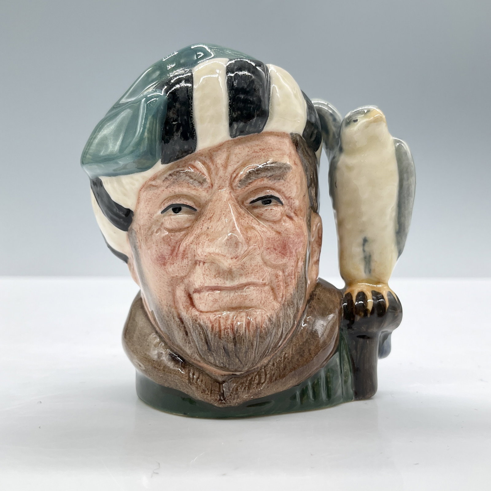 Falconer D6547 - Mini - Royal Doulton Character Jug: Variation One, green with black and white striped fur hat; green coat; grey and white falcon. Royal Doulton backstamp. Artist: Max Henk Dimensions: 2.5"L x 2"W x 2.75"H Date or Era: 1960 - 1991