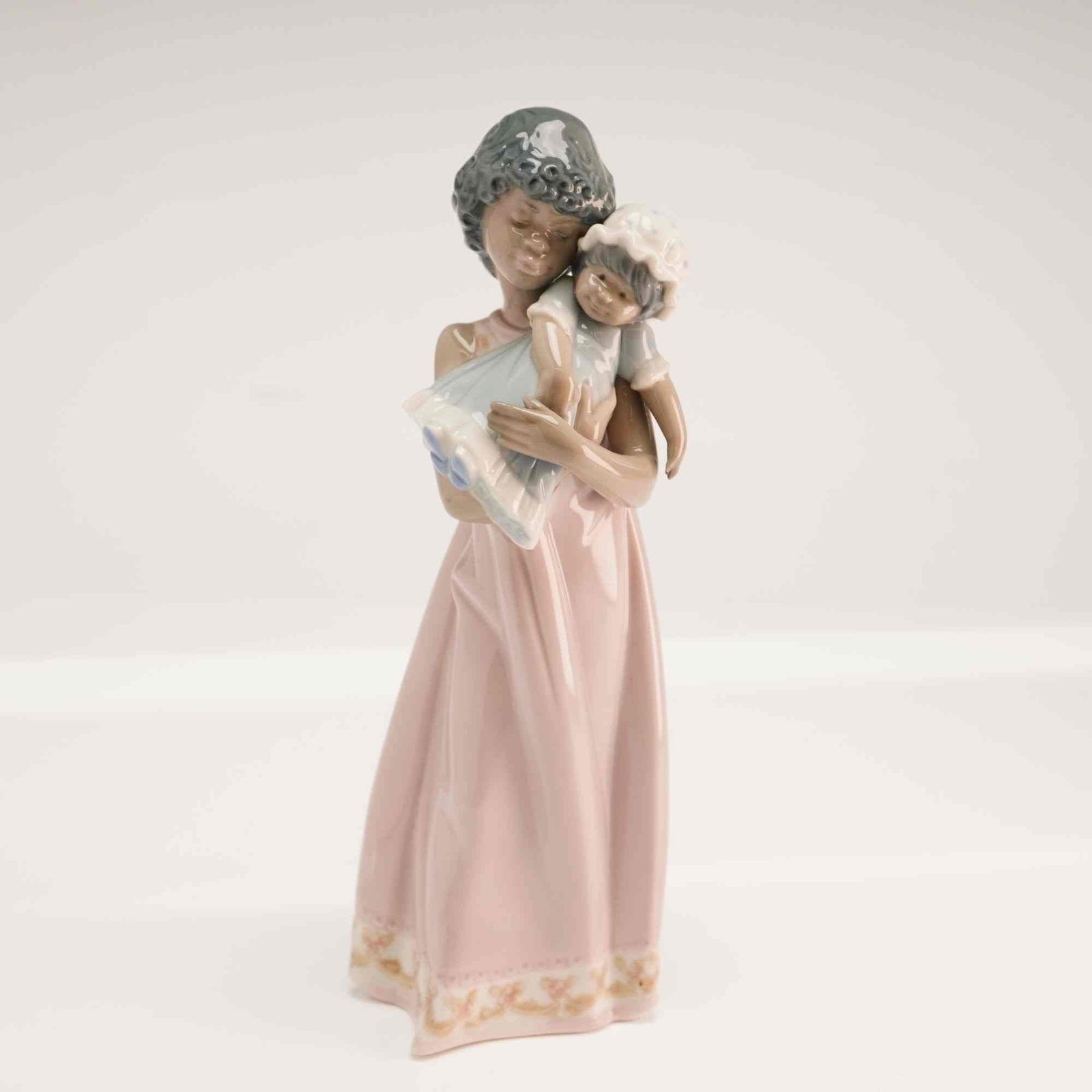 Lladro Baby Doll Glazed Porcelain Figurine Model 1005608: This Lladro glazed porcelain figurine is titled Baby Doll and is part of the maker's Black Legacy Collection. Designed by Juan Huerta and issued in 1989, the piece bears the model number 1005608. The 