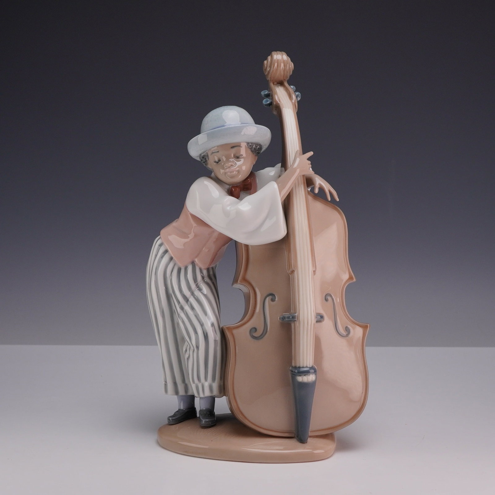 Lladro Black Legacy Porcelain Figurine Jazz Bass 1005834 with Box: Designed by sculptor Salvador Debon, the piece depicts a jazz musician in repose, leaning casually against a double bass. The figure is dressed in a blue-grey wide-brimmed hat, a white shirt with flar
