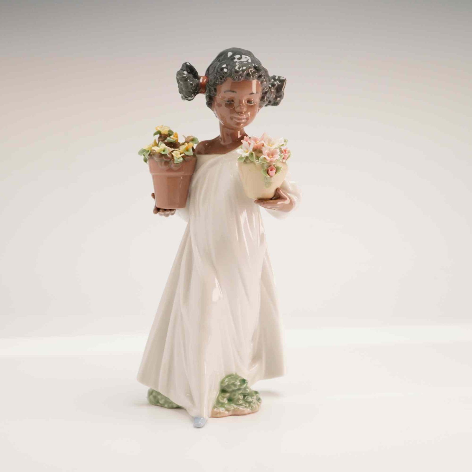 Lladro First Flowers Glazed Porcelain Figurine, Model 1006757 with Original Box: A Lladro glazed porcelain figurine titled First Flowers, model number 1006757. The piece depicts a young girl with her hair styled in two pigtails tied with red ribbons, wearing a flowing, off-the-sho