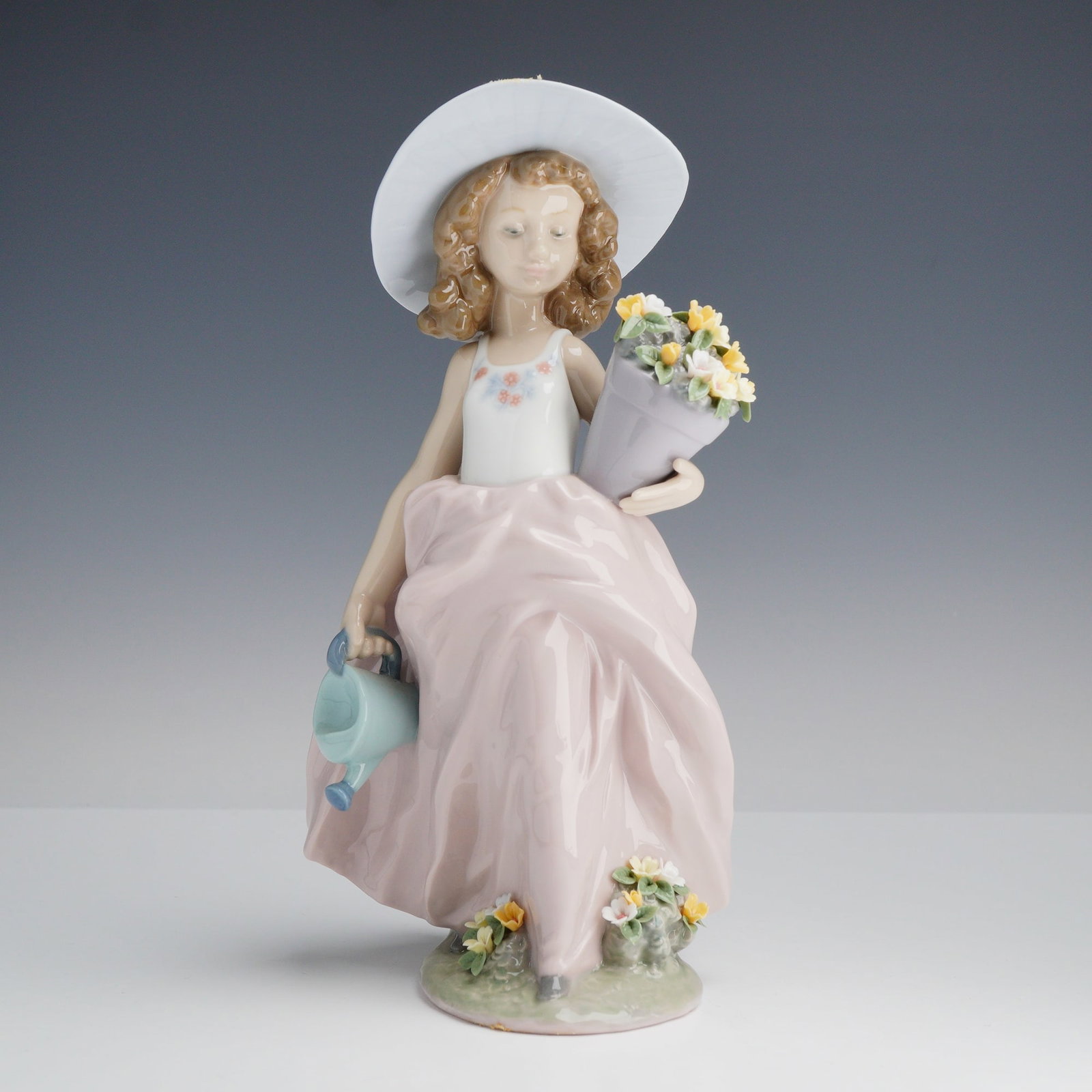 Lladro Porcelain Figurine A Wish Come True 01007676: A Lladro glazed porcelain figurine titled A Wish Come True, model number 7676. The polychrome figure depicts a young girl standing on a grass-textured base. She is wearing a wide-brimmed white hat acc
