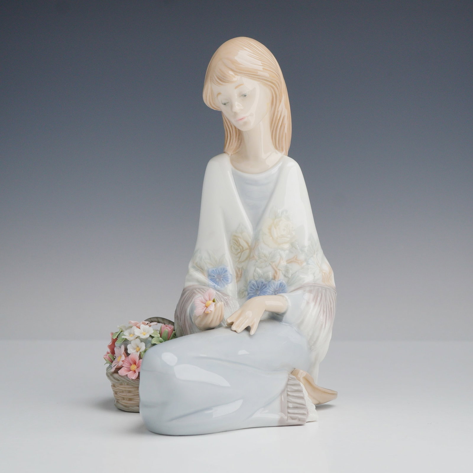 Lladro Porcelain Figurine Flower Song 01007607: A Lladro glazed porcelain figurine titled Flower Song, model number 7607. The piece depicts a young woman kneeling in a contemplative pose beside a basket filled with multi-colored blossoms. She has l