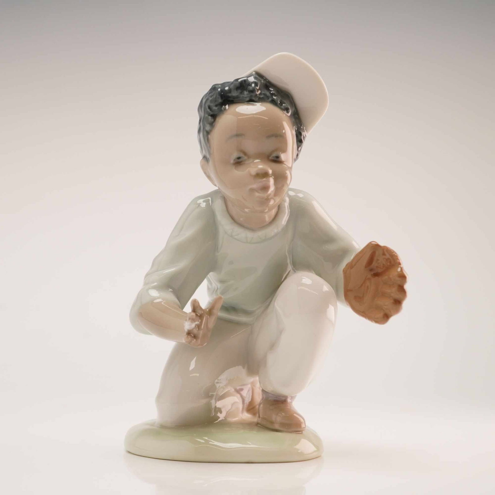Lladro Porcelain Figurine I've Got It Model 1005827: A Lladro glazed porcelain figurine titled I've Got It, model number 1005827, from the Black Legacy Collection. The figurine depicts a young boy in a crouching baseball catcher stance, wearing a light 