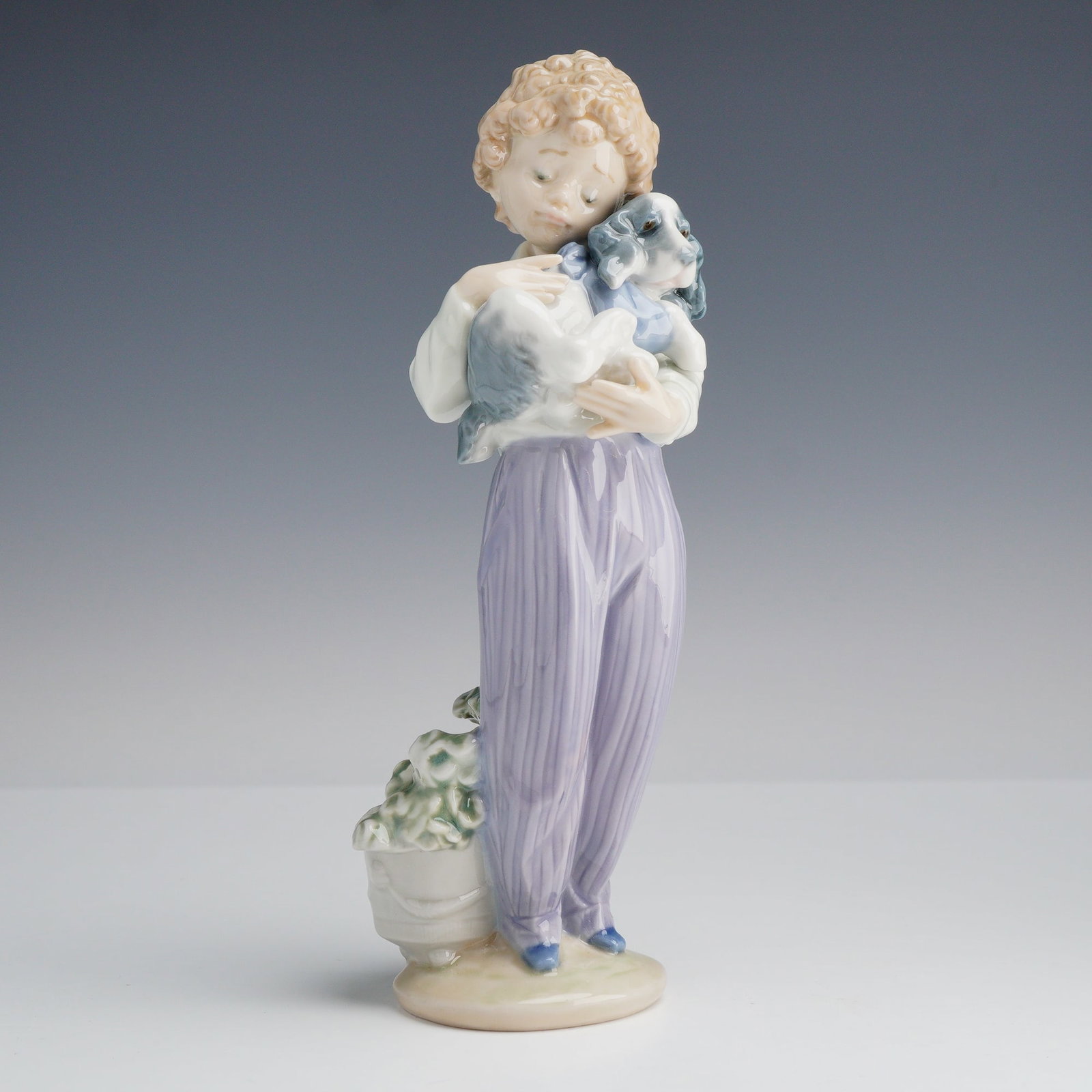 Lladro Porcelain Figurine My Buddy 01007609: This Lladro glazed porcelain figurine, titled My Buddy and designated as model number 7609, features a young boy with curly blond hair wearing a white collared shirt and lavender pinstriped trousers. 