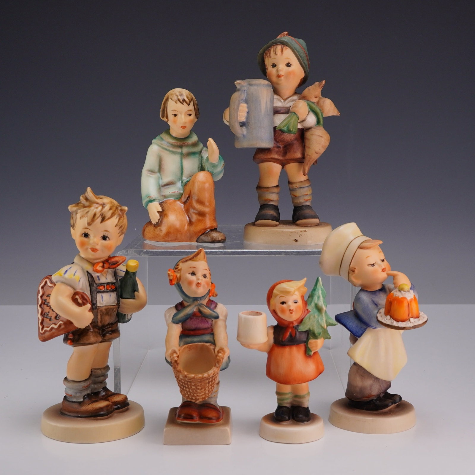 6pc Goebel M.I. Hummel Glazed Ceramic Figurines: This collection consists of six glazed polychrome ceramic figurines designed by M.I. Hummel and manufactured by Goebel in West Germany. Each piece depicts a child character in traditional European