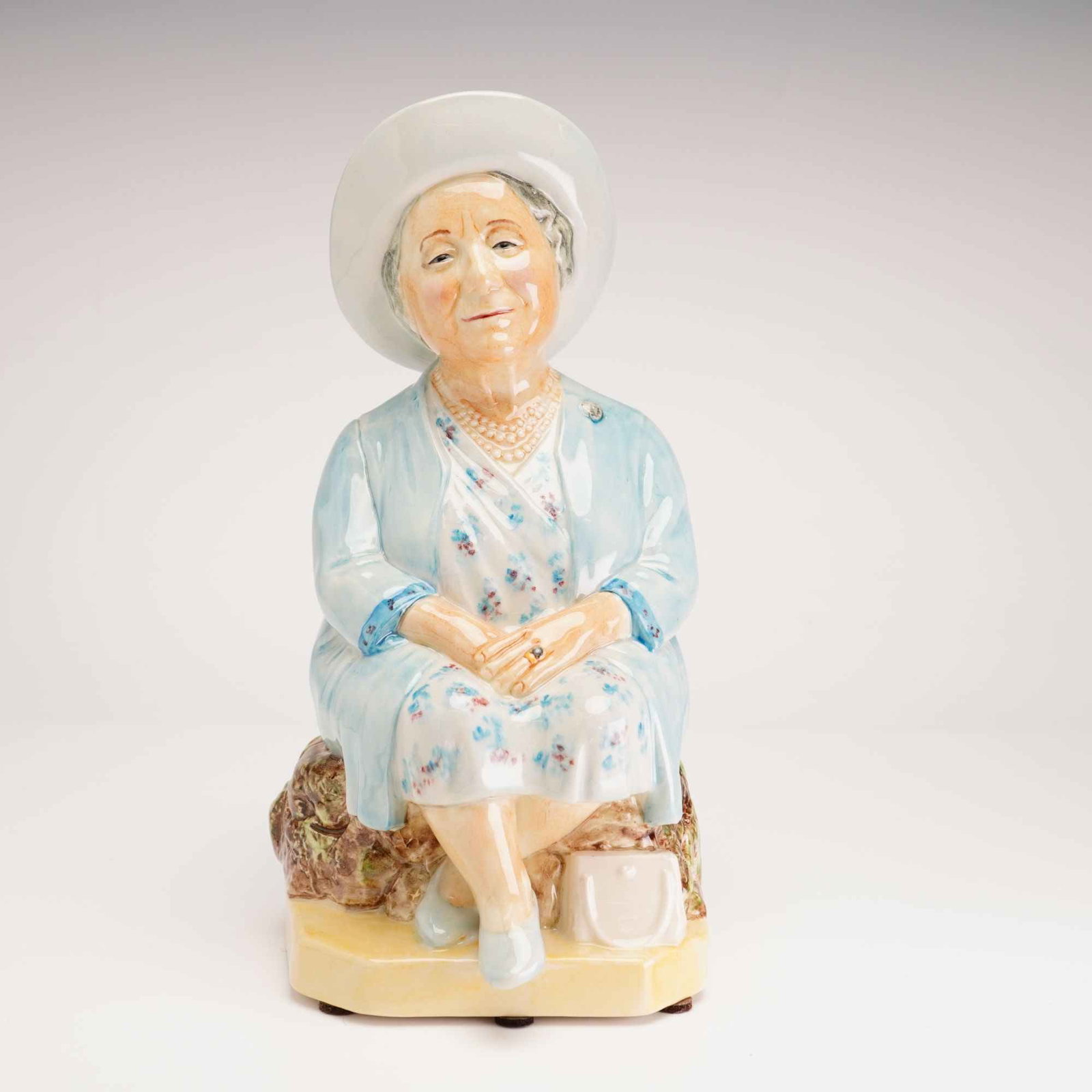 Kevin Francis Ceramics Commemorative Character Jug, The Queen Mother -Blue: A limited edition glazed ceramic character jug produced by Kevin Francis Ceramics, featuring a portrait of Her Majesty Queen Elizabeth The Queen Mother. The figure is seated on a rocky outcrop,
