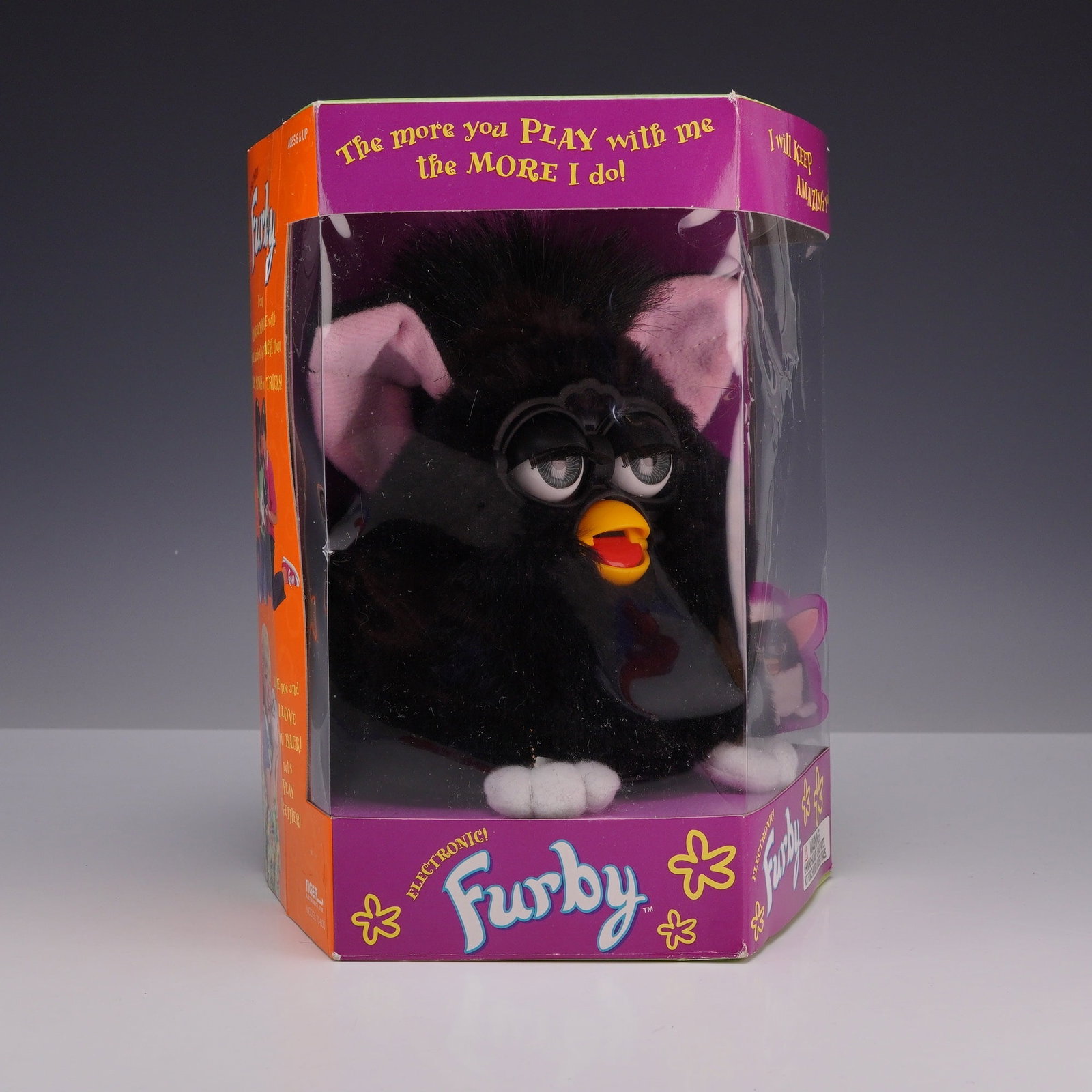 Vintage Tiger Electronics Model 70-800 Black and White Furby: The toy features solid black plush fur, white feet, and pink inner ears. The item remains secured within its original octagonal window box packaging. The original Furby paper tag is still attached to