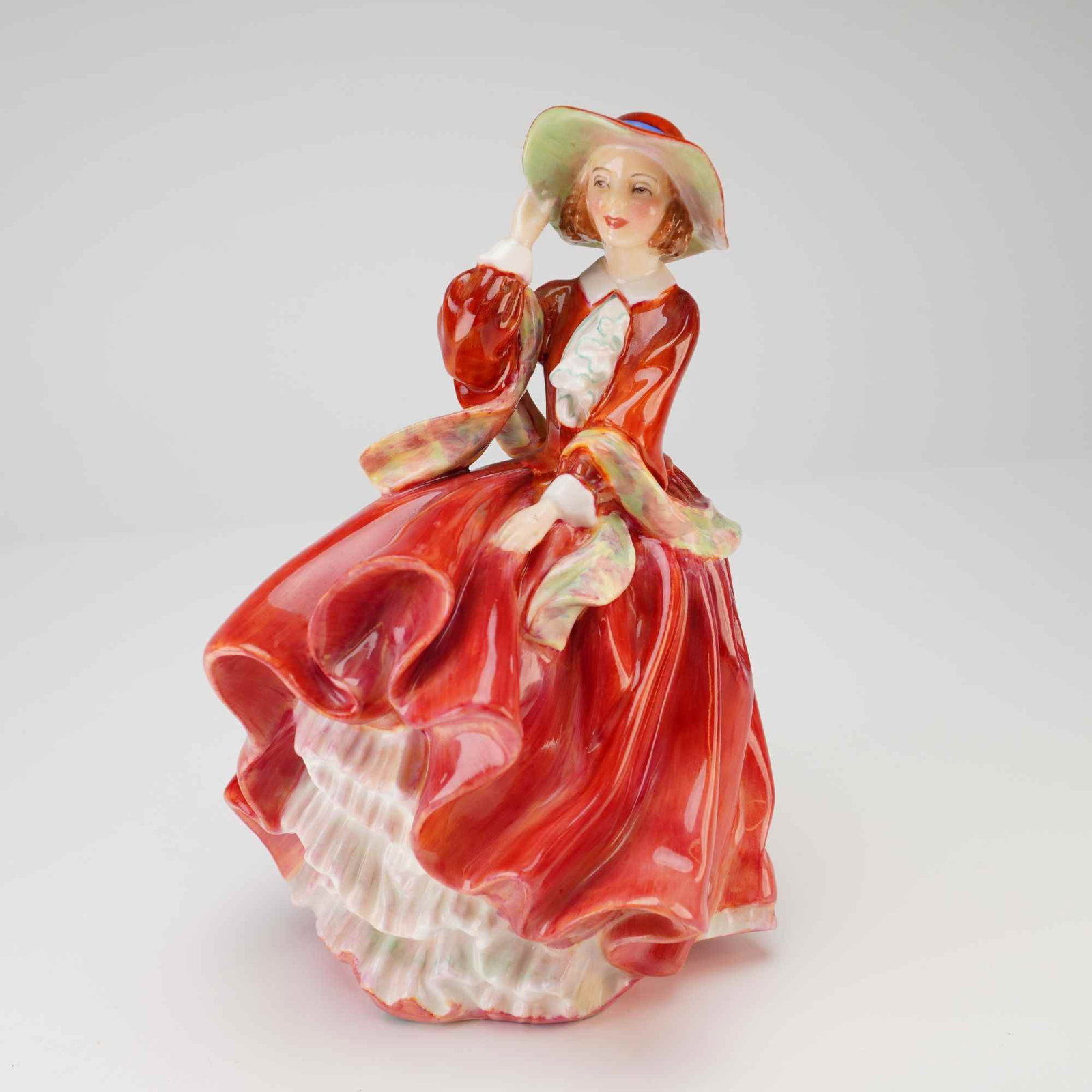 Royal Doulton Figurine, Top O'The Hill HN1834: A fine bone china Royal Doulton figurine titled Top o' the Hill, model number HN 1834. The piece depicts a young woman in a vibrant, wind-swept red dress with a ruffled white petticoat, clutching her 