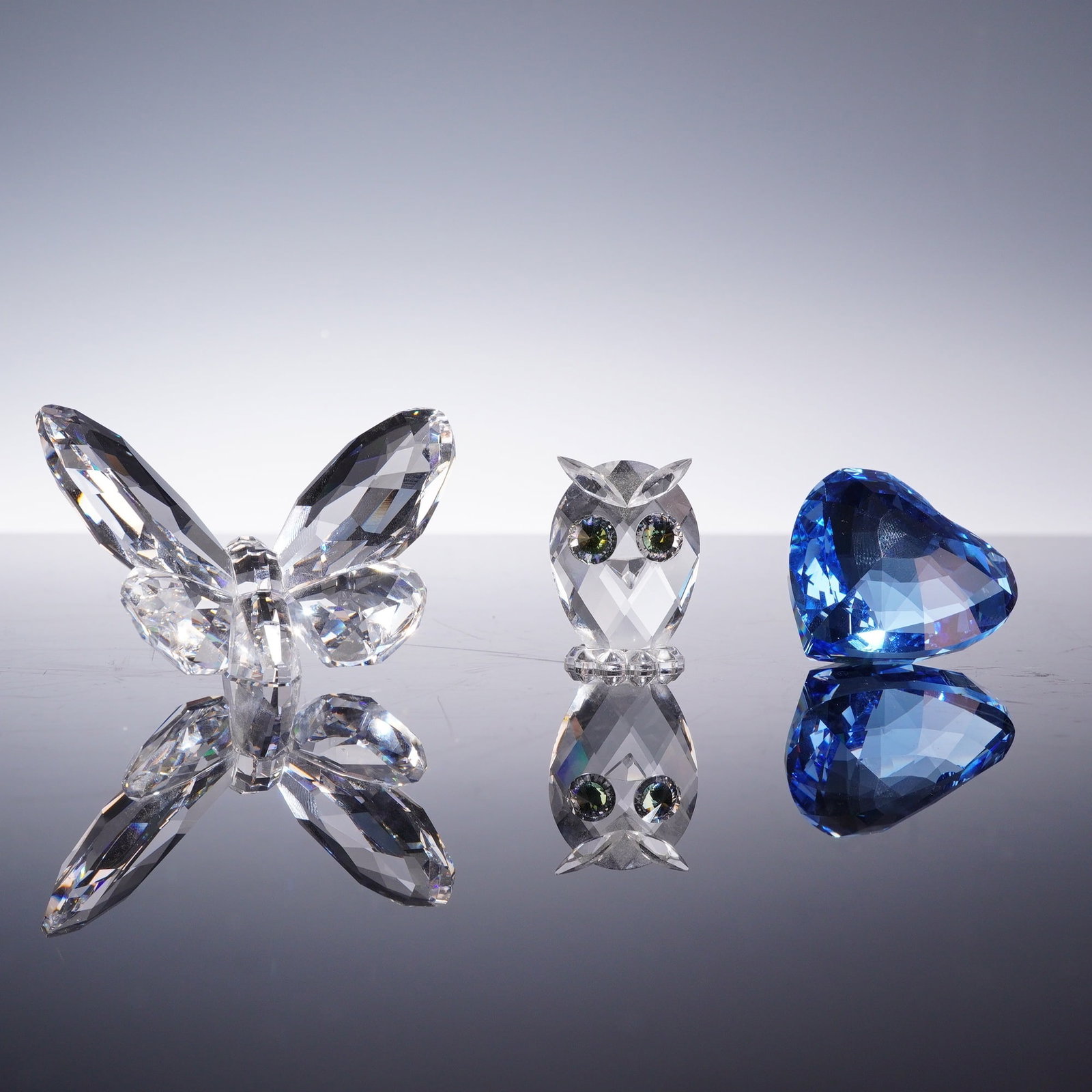 3pc Swarovski Crystal Figurines Including Owl, Heart Paperweight, and Butterfly: Swarovski lead crystal collection featuring an owl figurine, a heart-shaped paperweight, and a butterfly figurine. The owl is composed of faceted clear crystal with two yellow-brown faceted eyes and