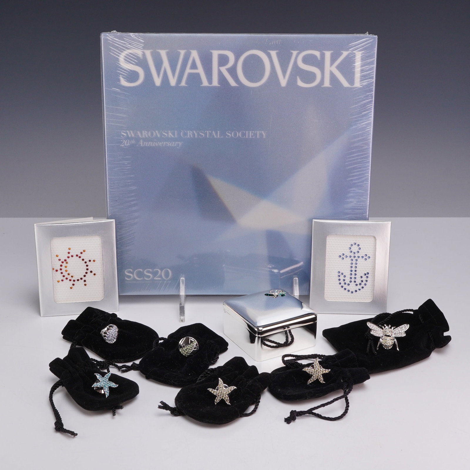 10pc Swarovski Crystal Society 20th Anniversary Collection Including Book Pins and Jewelry Box: This 10pc collection of Swarovski Crystal Society (SCS) commemorative items and jewelry is centered around the 20th anniversary of the society. The set includes one large blue-covered book titled