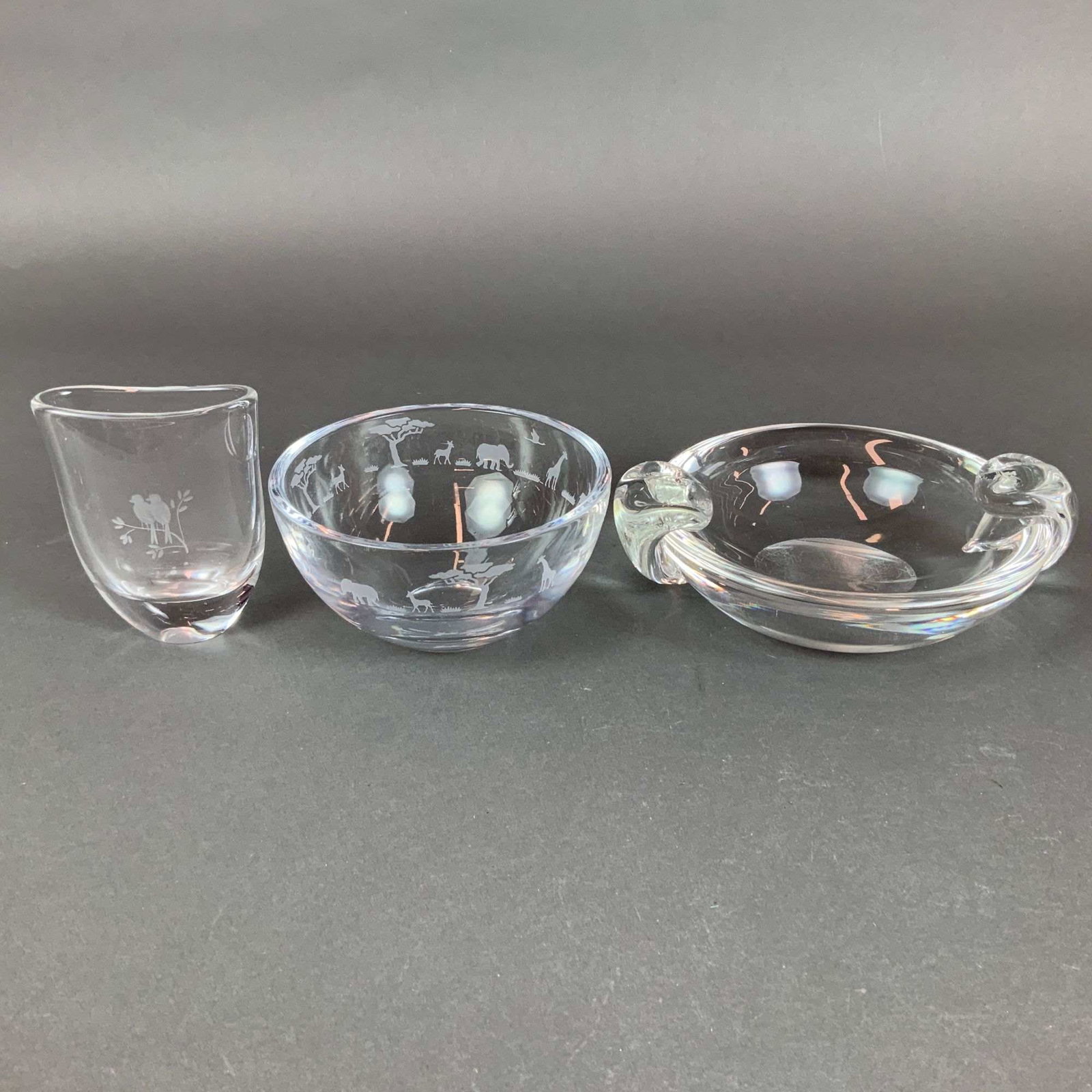 3pc Steuben and Orrefors Colorless Glass Bowls and Vase: This lot consists of three pieces of colorless decorative art glass featuring American and Scandinavian craftsmanship. The first item is a heavy Steuben crystal dish or ashtray designed with two