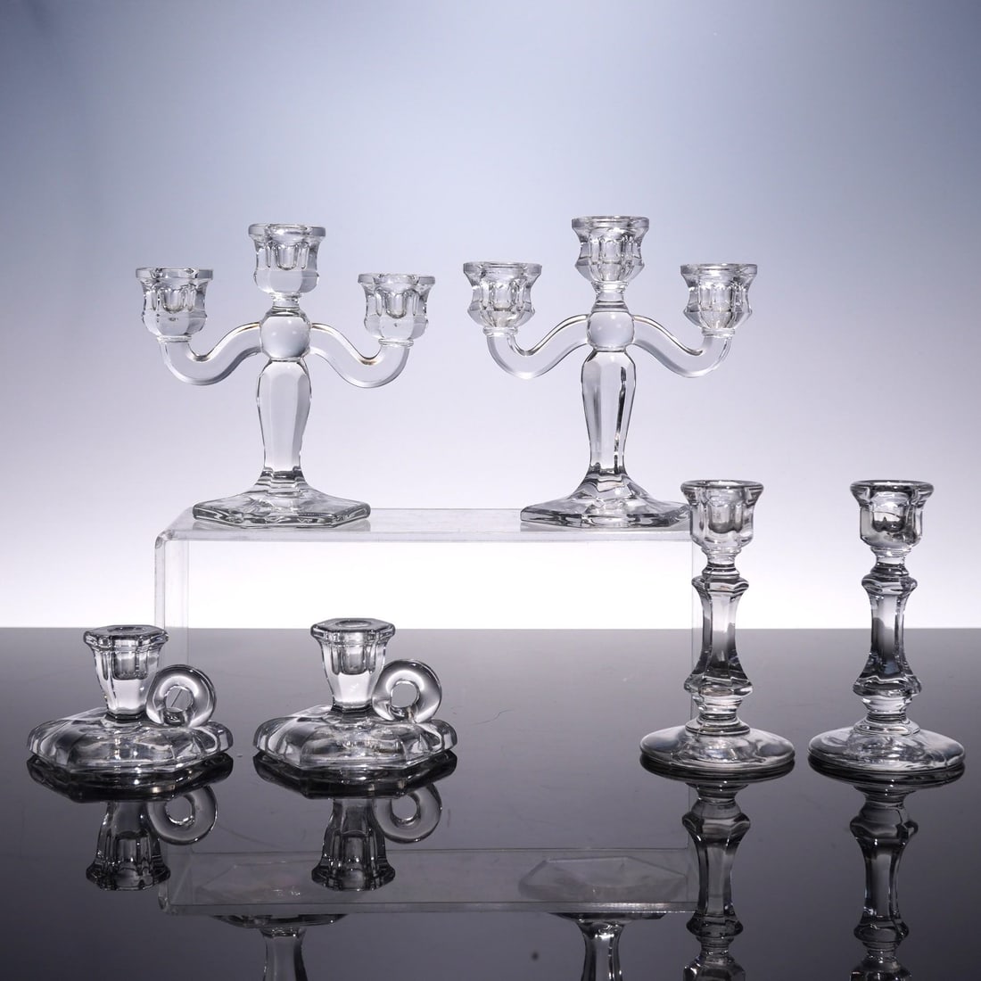 6pc Clear Glass Candlesticks: A charming mixed group of six clear pressed glass candlesticks, featuring three distinctive forms. Included are a pair of three-light candelabra with hexagonal bases and gracefully arched arms, a