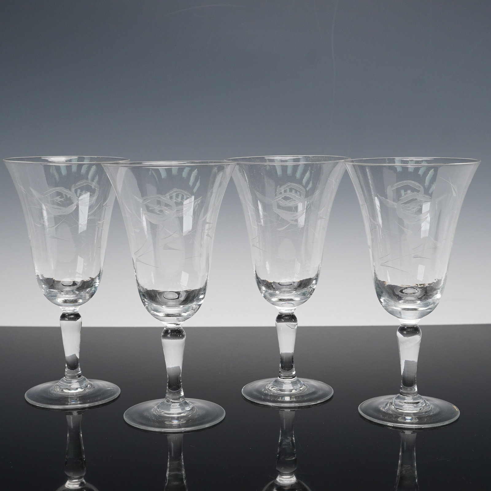 4pc Etched Crystal Floral Motif Water Goblets: A 4-piece set of etched crystal water goblets, each adorned with a subtle floral motif around the tall flared bowls. Resting on slender tapered stems and circular feet, these goblets offer both
