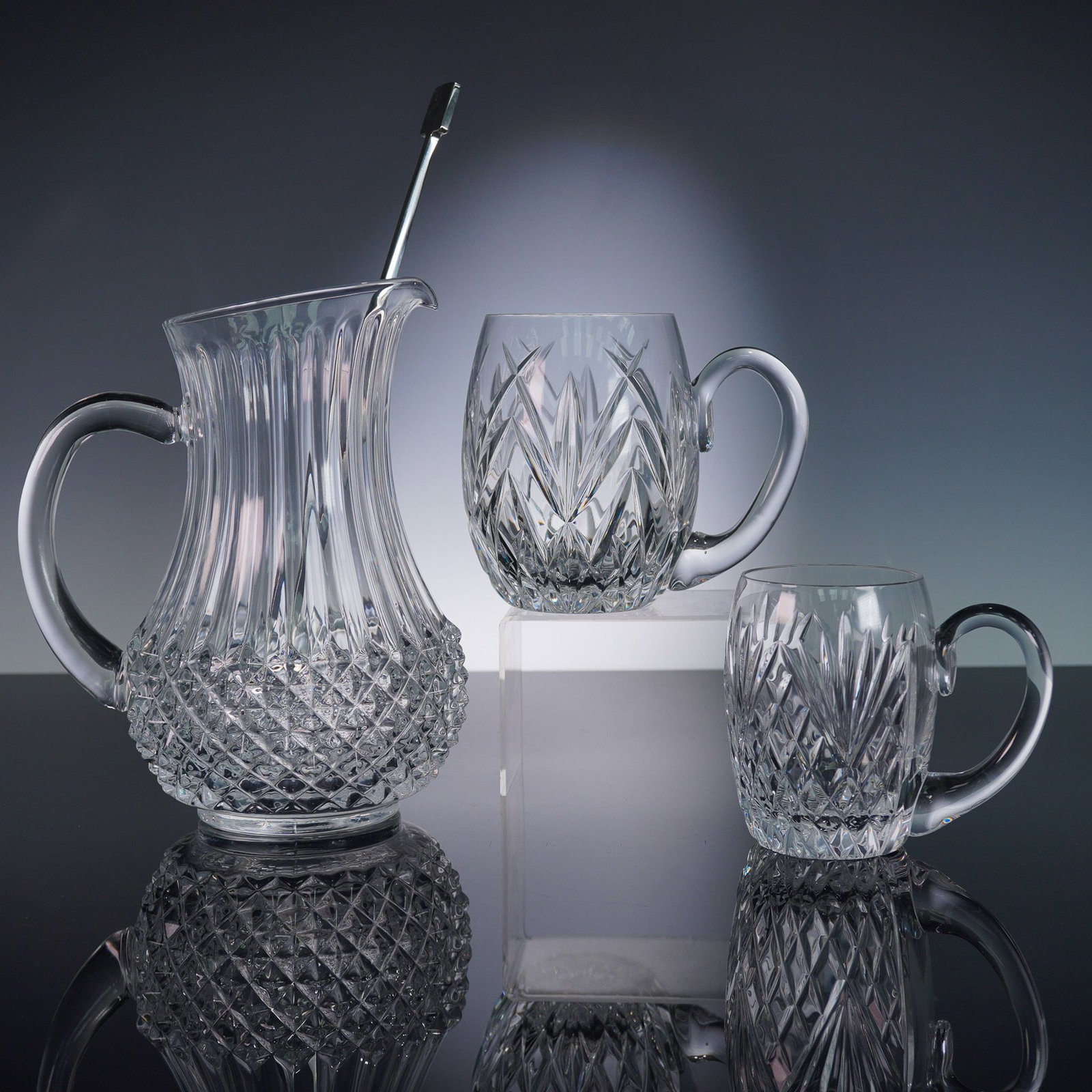 3pc Tyrone and Crystal D'Arques Jugs and Pitcher with Stainless Steel Stir: This mixed crystal barware lot features two Tyrone Crystal jugs in the iconic Tullamore and Antrim patterns, alongside a Cristal D'Arques Durand Longchamp pitcher. A sleek stainless steel stir stick i