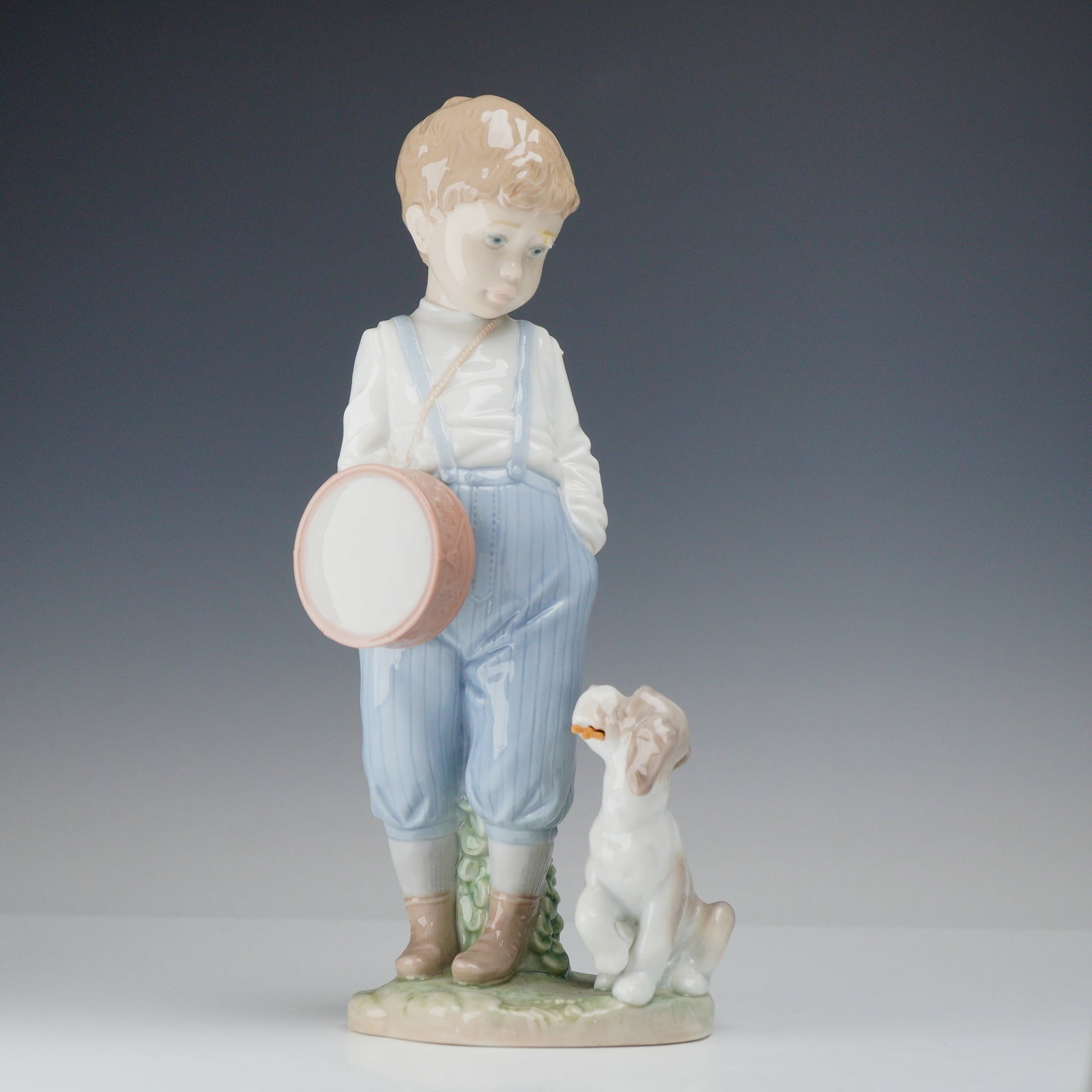 Lladro Friendly Duet Porcelain Figurine Model 6846: A Lladro glazed porcelain figurine titled Friendly Duet, model number 6846. This piece depicts a young boy in light blue pinstriped overalls and a white long-sleeved shirt standing with his hands in