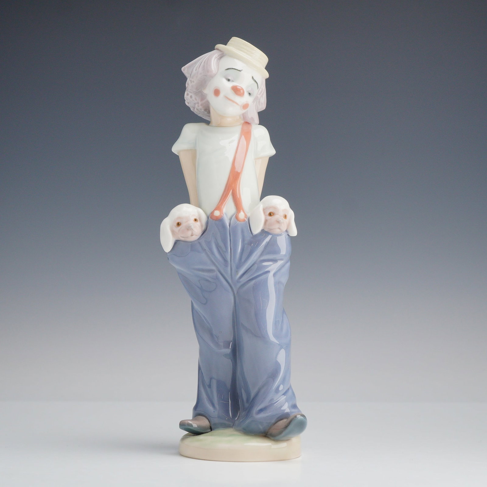 Lladro Glazed Porcelain Figurine Little Pals 01007600: A glazed porcelain figurine manufactured by Lladro, titled Little Pals (Pequenos Colegas). This piece was designed by sculptor Juan Huerta and depicts a melancholy circus clown in a classic