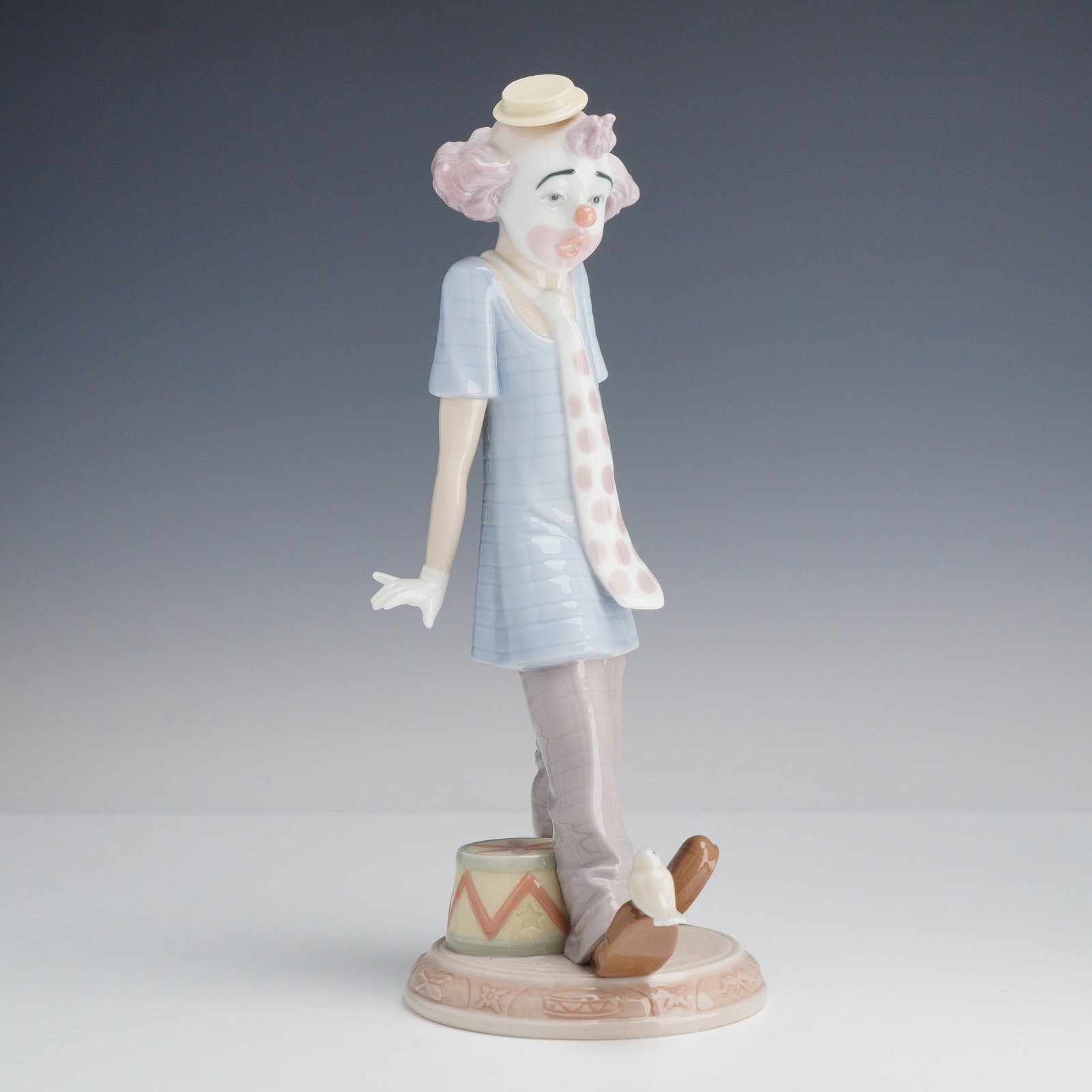 Lladro Porcelain Figurine Circus Days 01006916: This glazed porcelain figurine is a Lladro production titled Circus Days, model number 6916. Handmade in Spain, the piece depicts a whimsical clown in a pensive stance. The figure is designed with pin