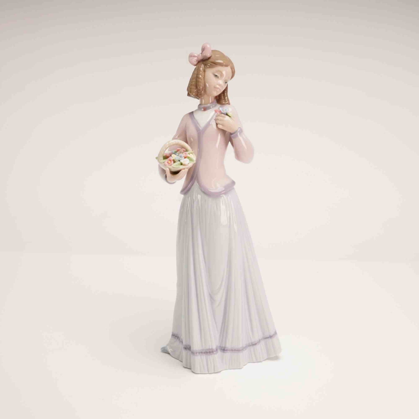 Lladro Porcelain Figurine Innocence in Bloom 01007644 with Box: Produced in 1996 as a Collectors Society annual edition, the piece depicts a young woman in a long, pleated greyish-blue skirt with a purple decorative band at the hem and a pale pink jacket over a wh