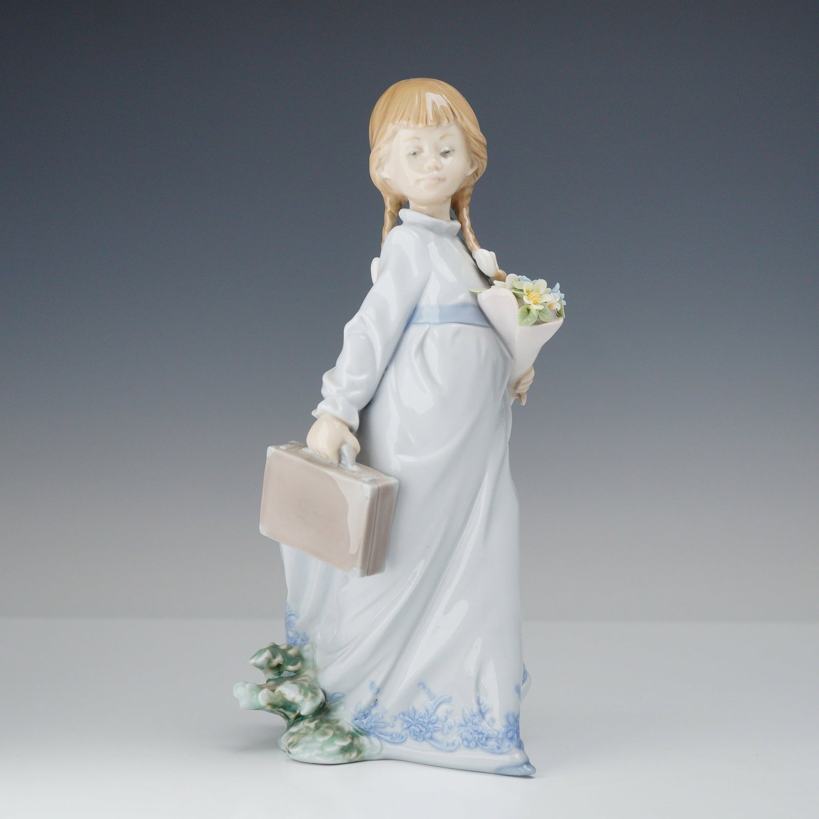 Lladro Porcelain Figurine School Days 01007604: This glazed porcelain figurine by Lladro is titled School Days, model number 7604, and was issued in 1988 for the Lladro Collectors Society. The piece depicts a young girl with blonde hair styled in p