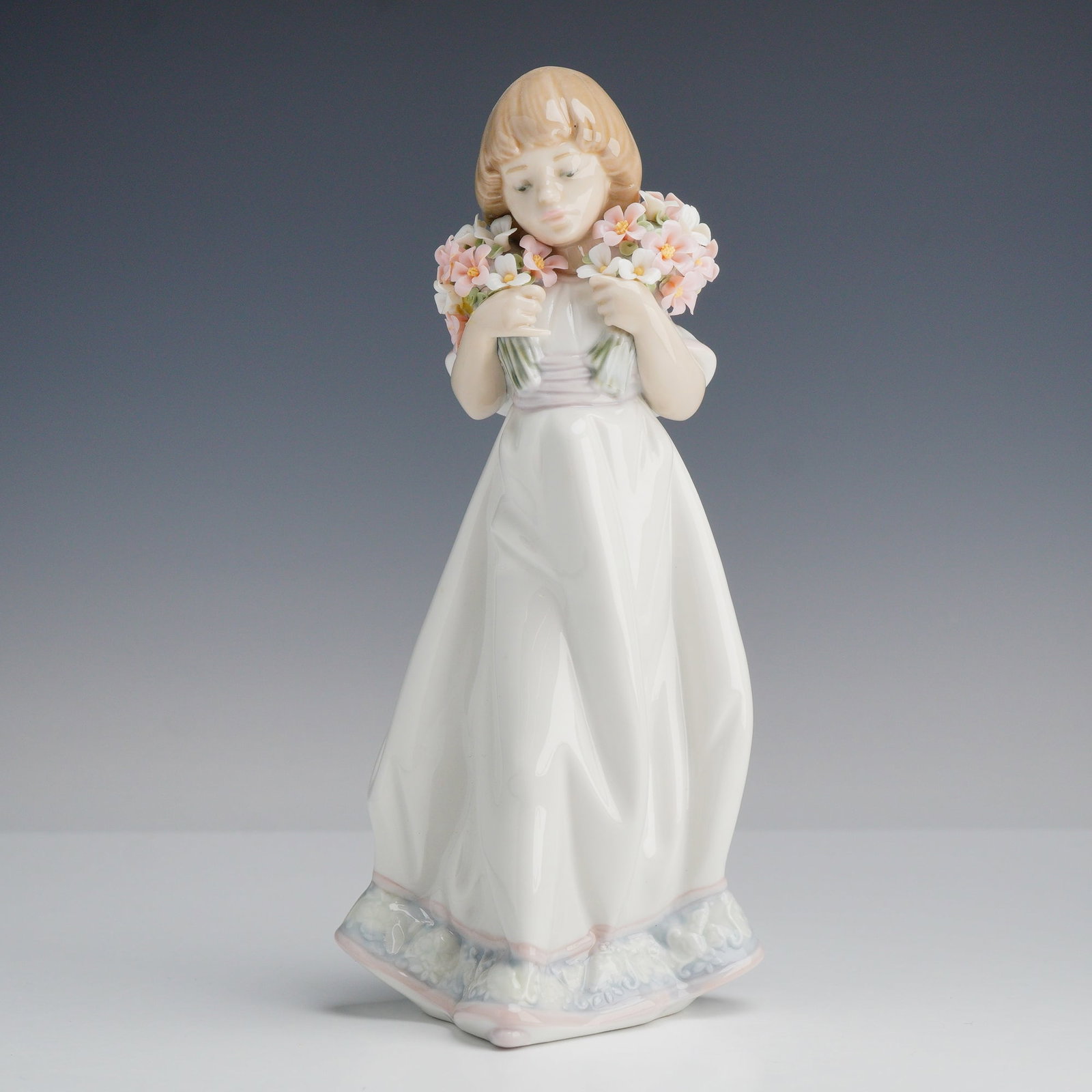 Lladro Porcelain Figurine Spring Bouquets 01007603: This Lladro glazed porcelain figurine, model number 7603, is titled Spring Bouquets and was designed by artist Jose Puche. The piece depicts a young girl with shoulder-length blonde hair holding clust