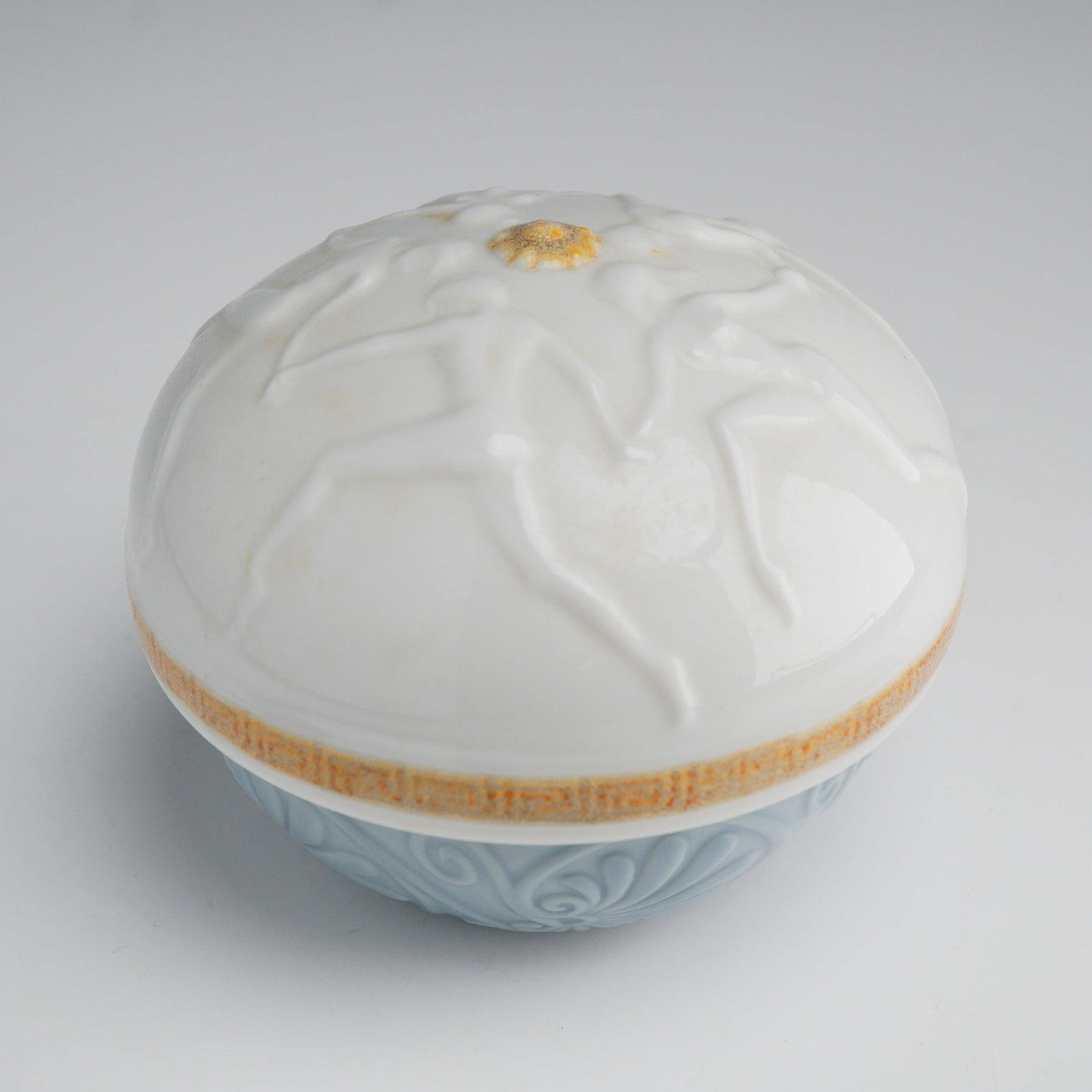 Lladro Privilege Gold Greek Dancers Porcelain Trinket Box 01007705: A Lladro porcelain trinket box from the Privilege Gold collection, model number 7705, titled Greek Dancers. This circular lidded box is composed of a domed white porcelain lid and a light blue porcela