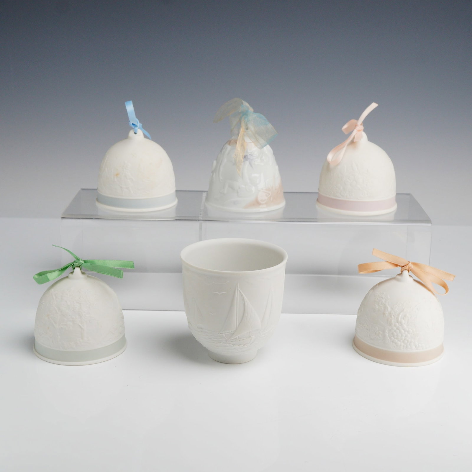 6pc Lladro Collectors Society White Bisque Porcelain Bells and Vessel: A collection of six white matte bisque porcelain pieces from the Lladro Collectors Society, manufactured in Spain. The group consists of five annual Christmas bells and one commemorative vessel. Each 