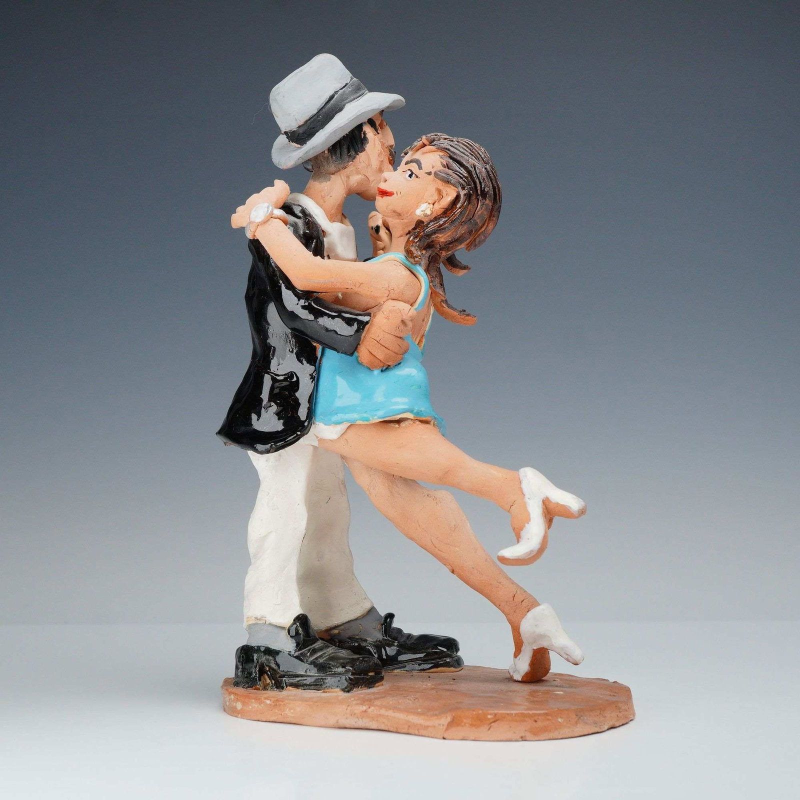 Handmade Clay Sculpture Figurine Depicting a Dancing Couple: A whimsical, hand-modeled ceramic figurine depicting a couple in a dramatic tango dance pose. The male figure is portrayed with a mustache, wearing a gray fedora-style hat, a glossy black jacket, and 