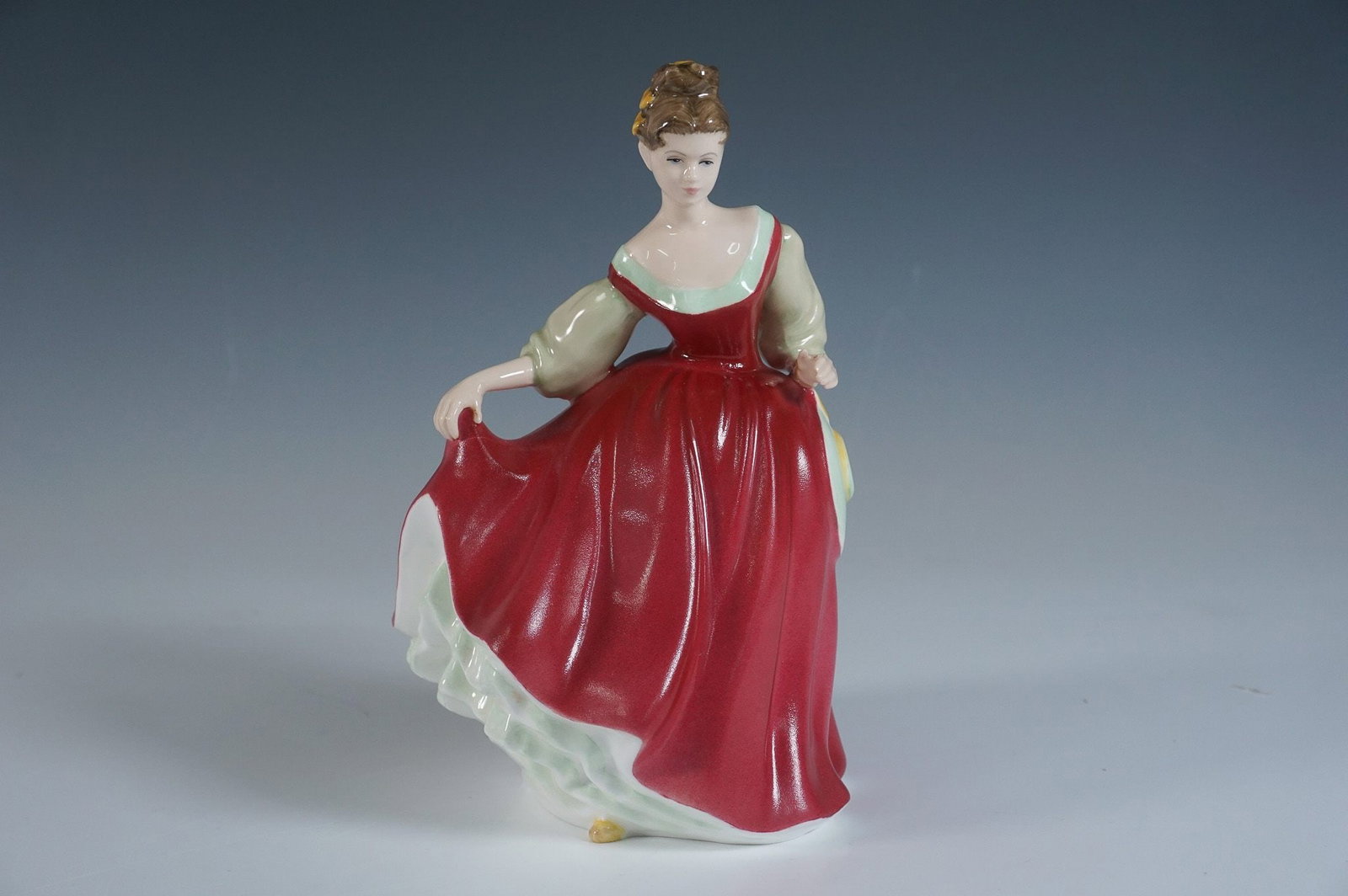 Royal Doulton Figurine Fair Lady HN 2832, Red, Boxed: A graceful and finely detailed Royal Doulton figurine, Fair Lady HN 2832, designed by Peggy Davies. This elegant piece showcases a poised lady in a flowing crimson-red gown, lifting her skirt slightly