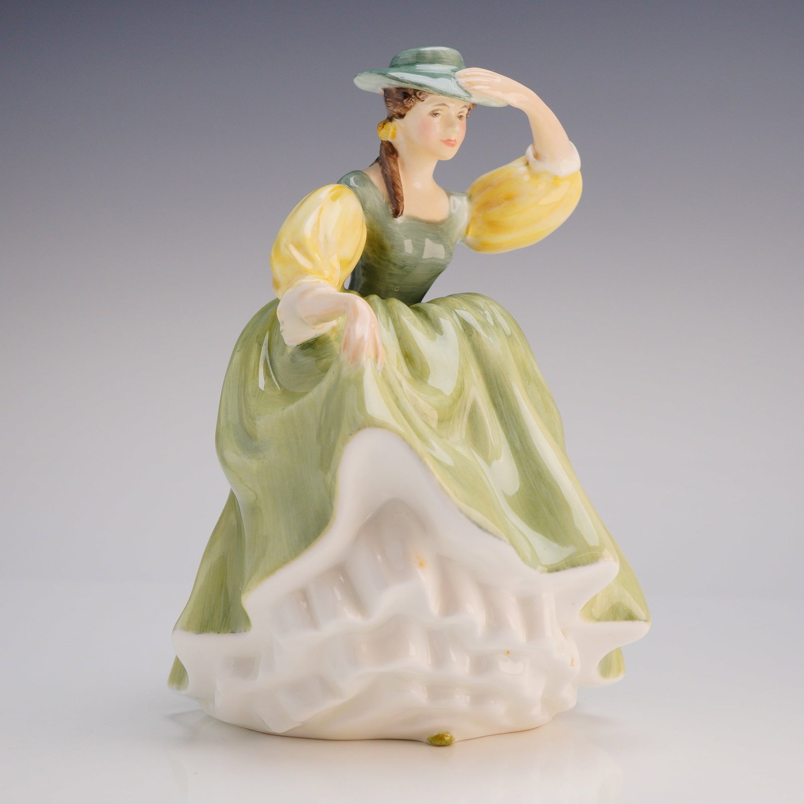 Royal Doulton Figurine Buttercup HN 2309: The figure depicts a woman in a voluminous period-style dress, posed with one hand raised, possibly shading her eyes or adjusting her hat. The figurine is hand-painted with soft greens and lime yellow