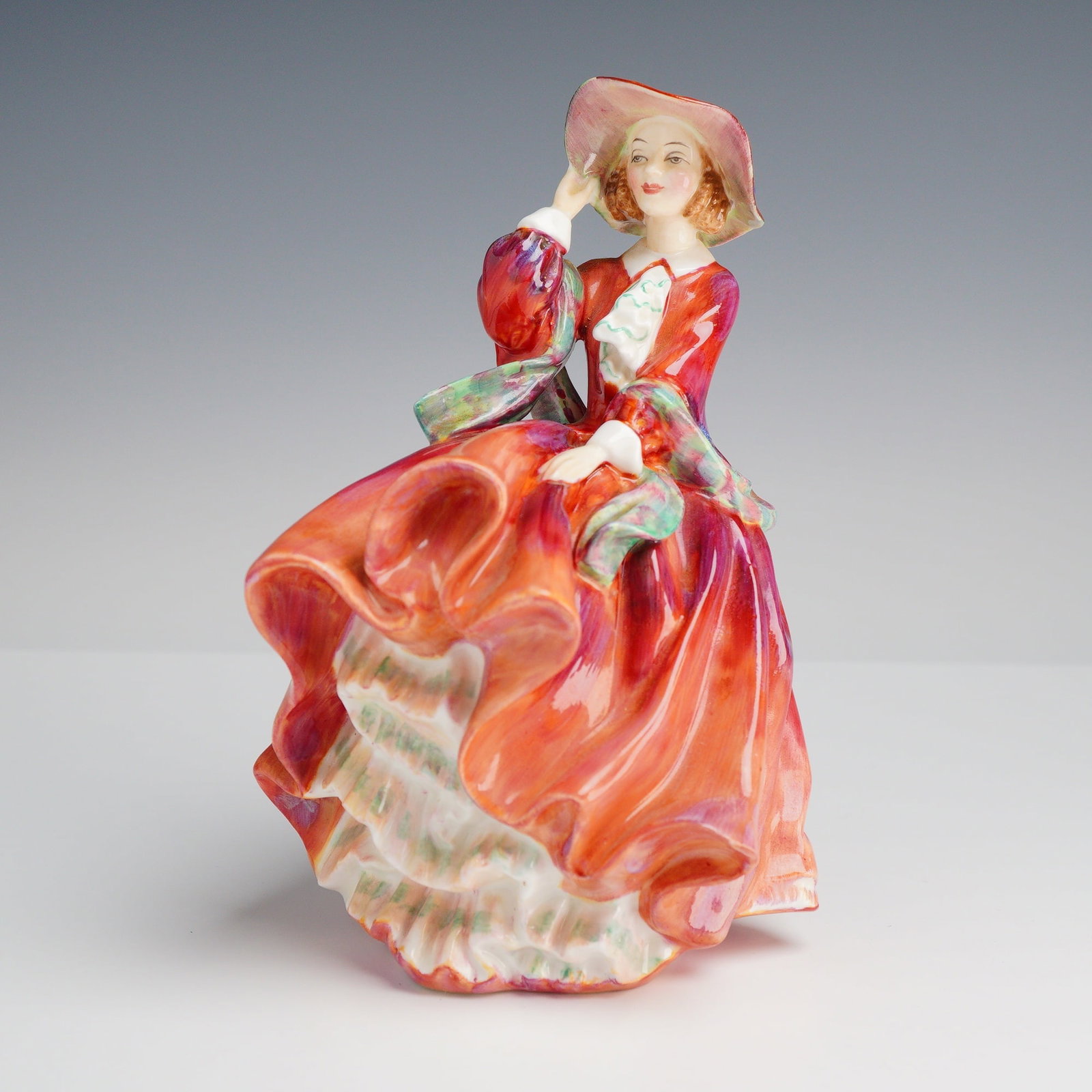 Royal Doulton, Top O the Hill Figurine: This Royal Doulton fine bone china figurine, titled Top o' the Hill and numbered HN1834, was designed by artist Leslie Harradine. The subject is a young woman wearing a vibrant, wind-swept dress in va