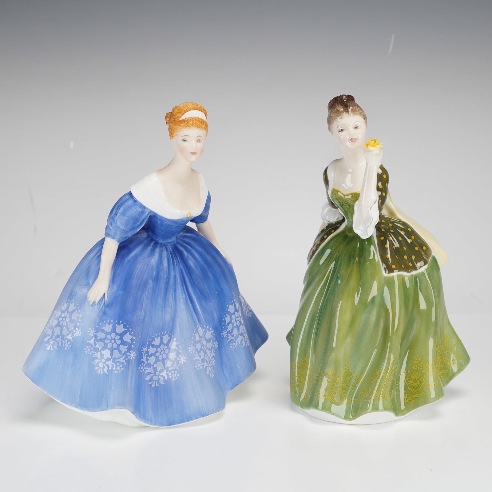 Two Royal Doulton Bone China Figurines Nina HN 2347 & Fleur HN 2368: This lot features two Royal Doulton glazed bone china figurines. The first figurine is titled Nina, model number HN 2347. The figure is depicted in a mid-19th-century style blue gown with white floral