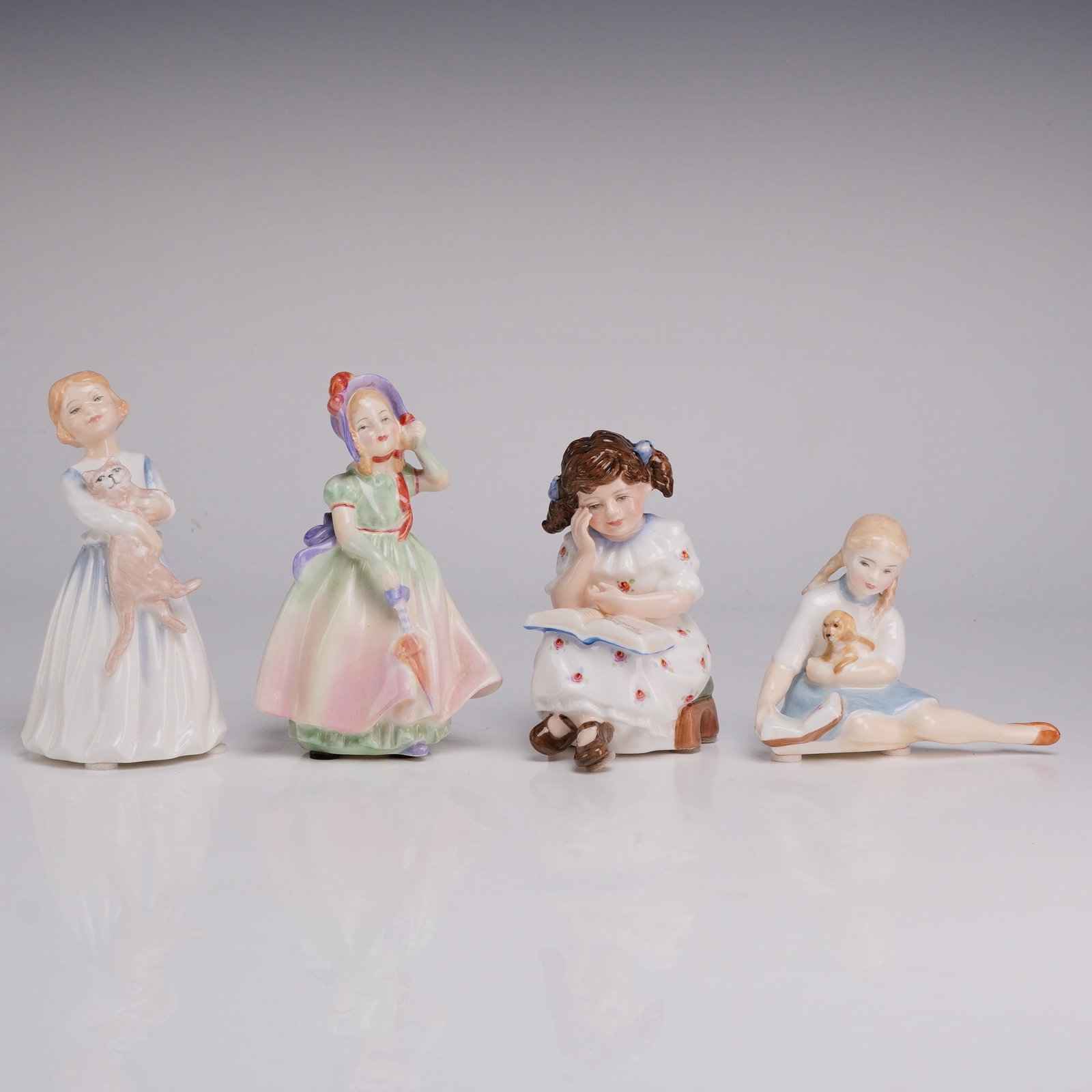 Four Royal Doulton Figurines- Babie HN1679, My First Pet 3122, Story Time 3695 & My Pet 2238: A collection of four hand-painted glazed porcelain figurines produced by Royal Doulton in England, each depicting a young girl in a distinct pose. The first figurine, My First Pet (HN 3122), features 