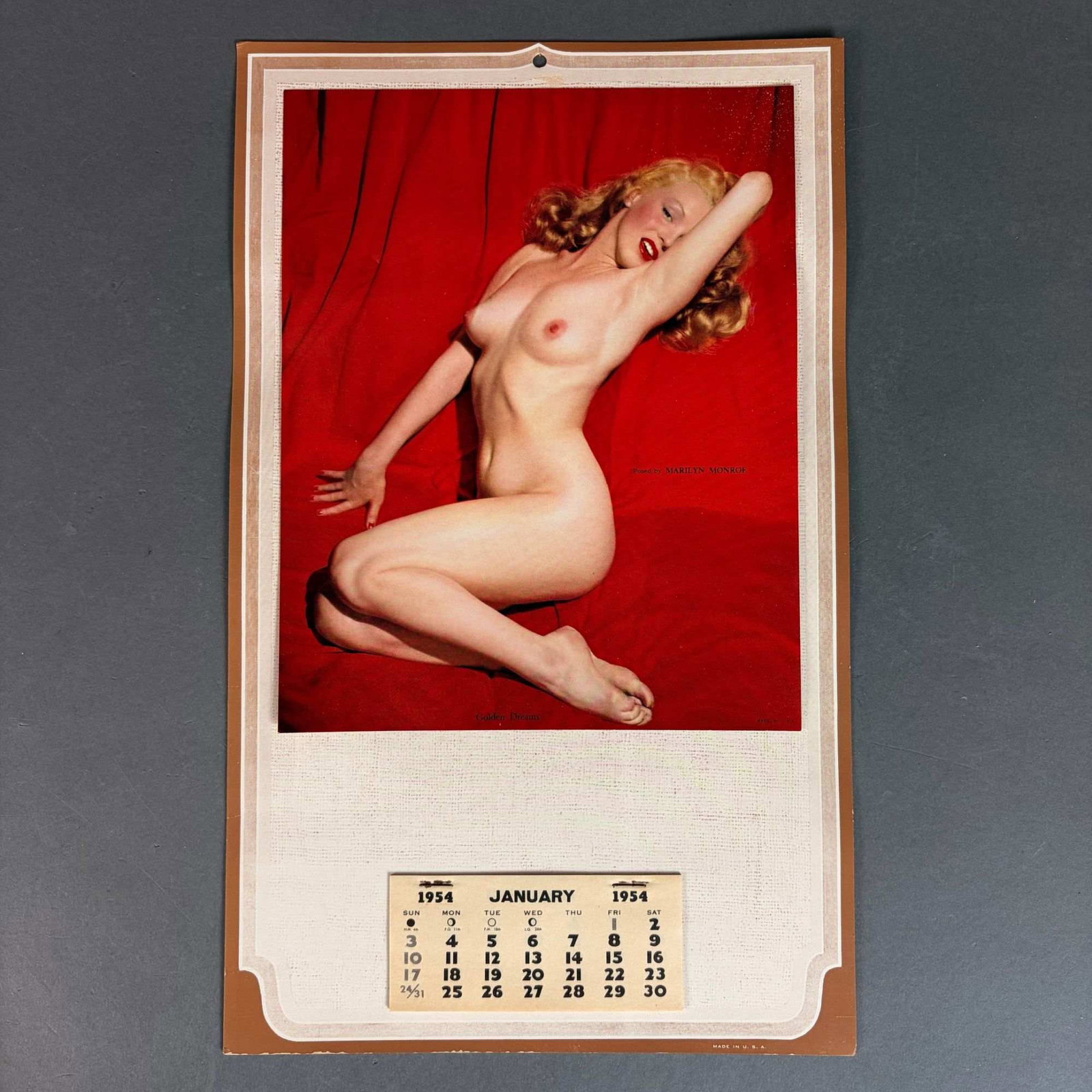 1954 Marilyn Monroe Golden Dreams Pin-Up Calendar: This vintage wall calendar from 1954 features the Golden Dreams nude photograph of Marilyn Monroe. The image, originally captured by photographer Tom Kelley in 1949, depicts Marilyn reclining against 