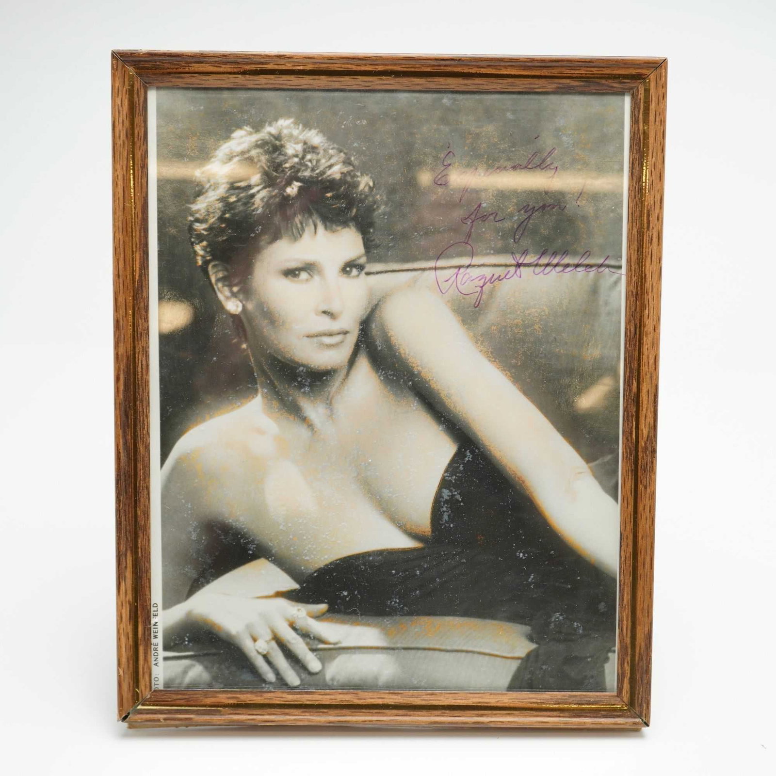 Raquel Welch Autographed Photograph by Andre Weinfeld: An autographed photo of Raquel Welch, captured by photographer Andre Weinfeld. The black and white portrait depicts the actress with a short hairstyle, wearing a dark strapless gown and a prominent ri