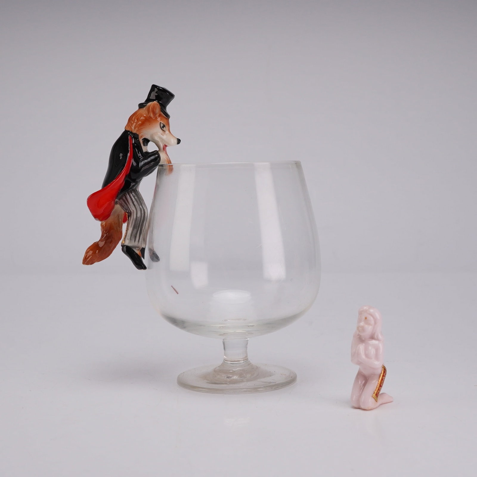 Mid-Century Japanese Novelty Barware w/ Fox Glass Sitter & Surprise Nude Figurine: This mid-century novelty barware set includes a clear glass brandy snifter, two hand-painted glazed ceramic figurines, and an original presentation box. The primary figurine is an anthropomorphic fox 