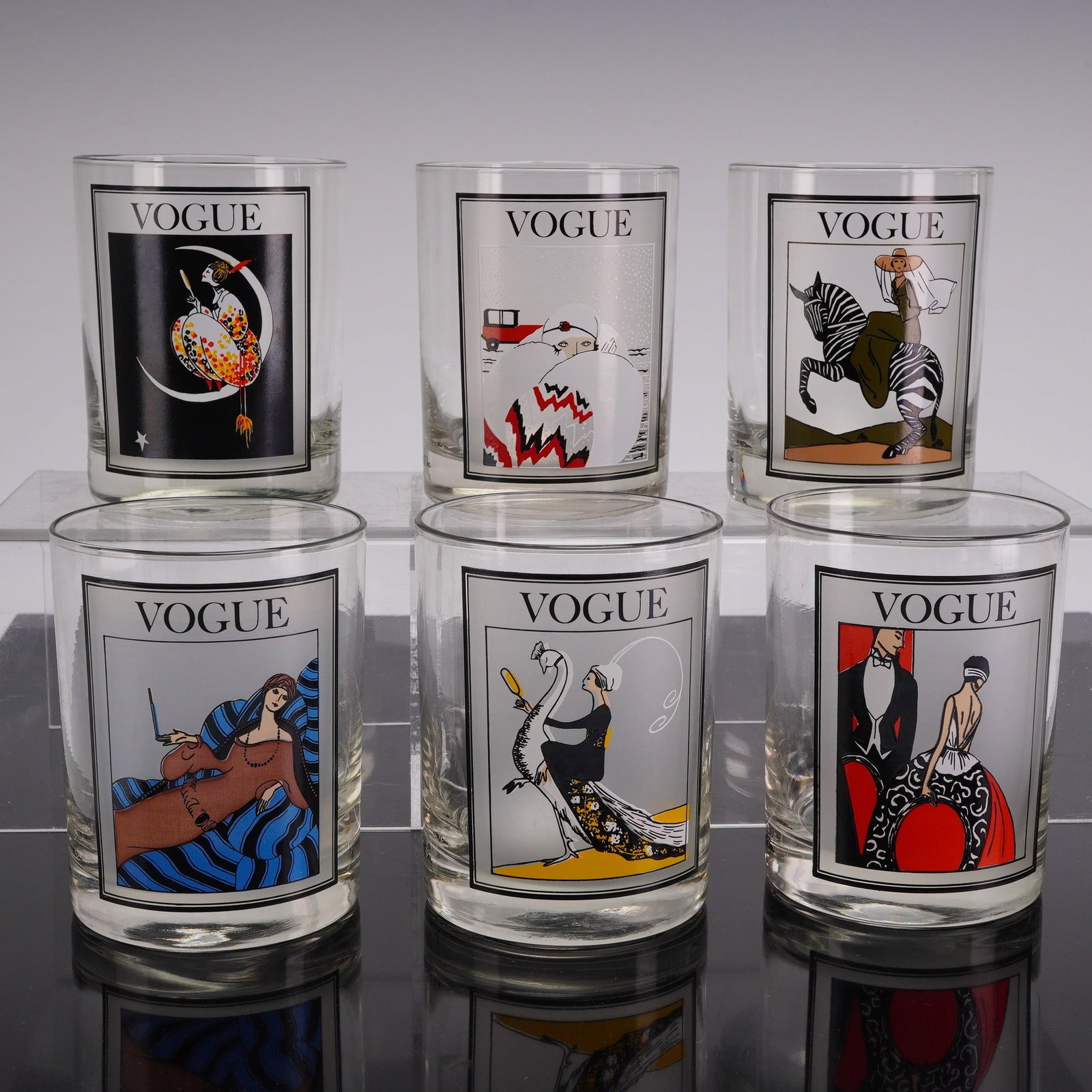 Set of 6 Vintage Cera Vogue Cover Bar Glasses: A set of six clear glass lowball tumblers. Each glass features a unique multi-color screen-printed illustration inspired by early 20th-century fashion magazine covers. The designs are enclosed in a
