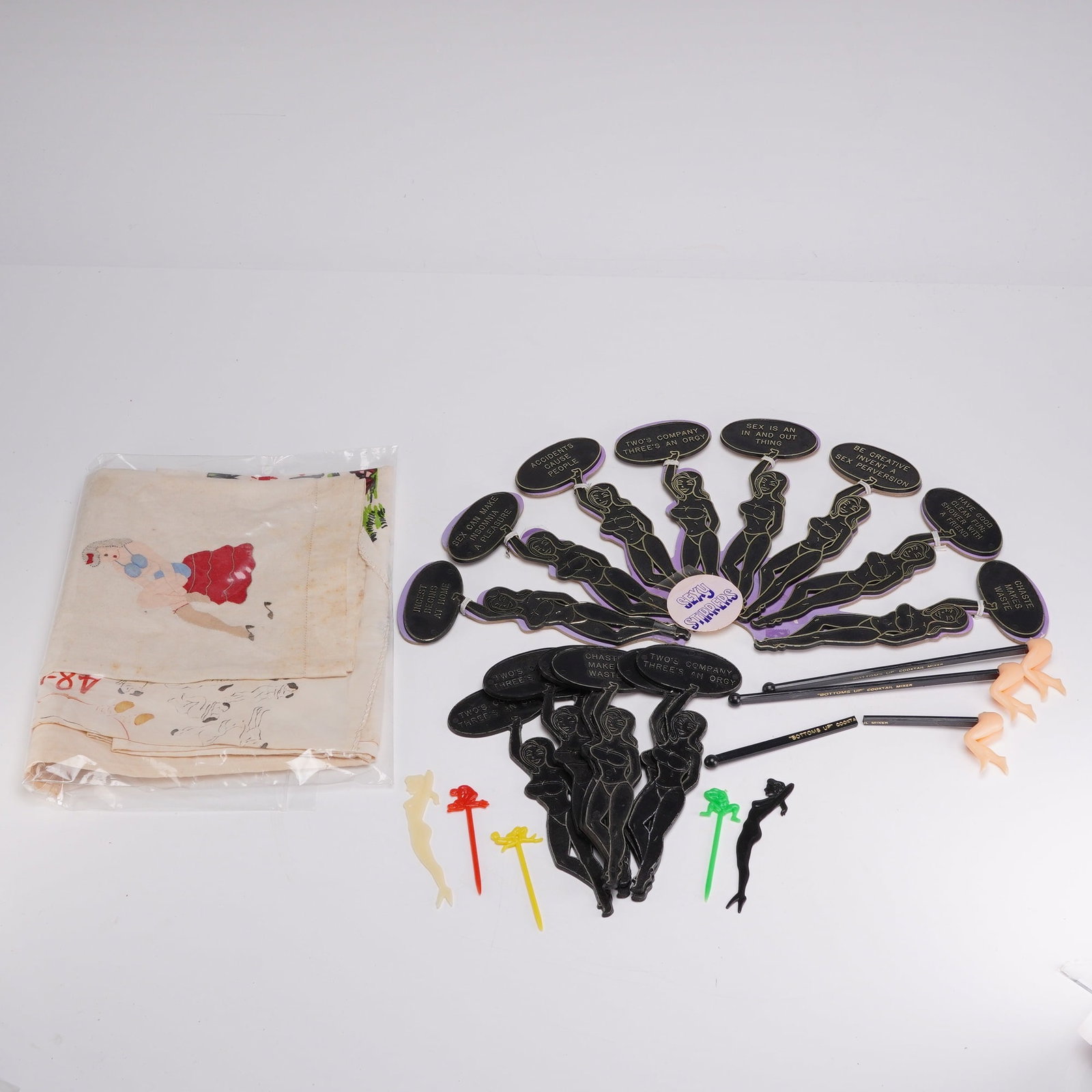 17pc Mid-Century Adult Novelty Ephemera and Barware Accessories: This collection of mid-20th-century adult novelty ephemera includes barware accessories and printed textiles. The group features a printed pin-up textile depicting a central figure in a red skirt and