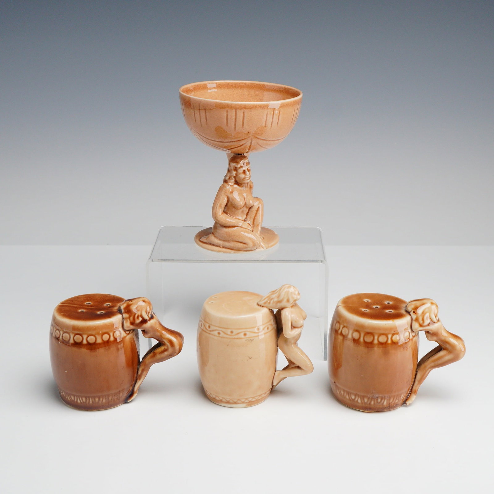 Group of Four Dorothy Kindell Strip Tease Series Ceramic Nude Shakers and Coupe: This four-piece group of ceramic nude shakers and coupe is attributed to Dorothy Kindell from the Strip Tease barware series. The collection includes one stemmed coupe and three barrel-form shakers. E