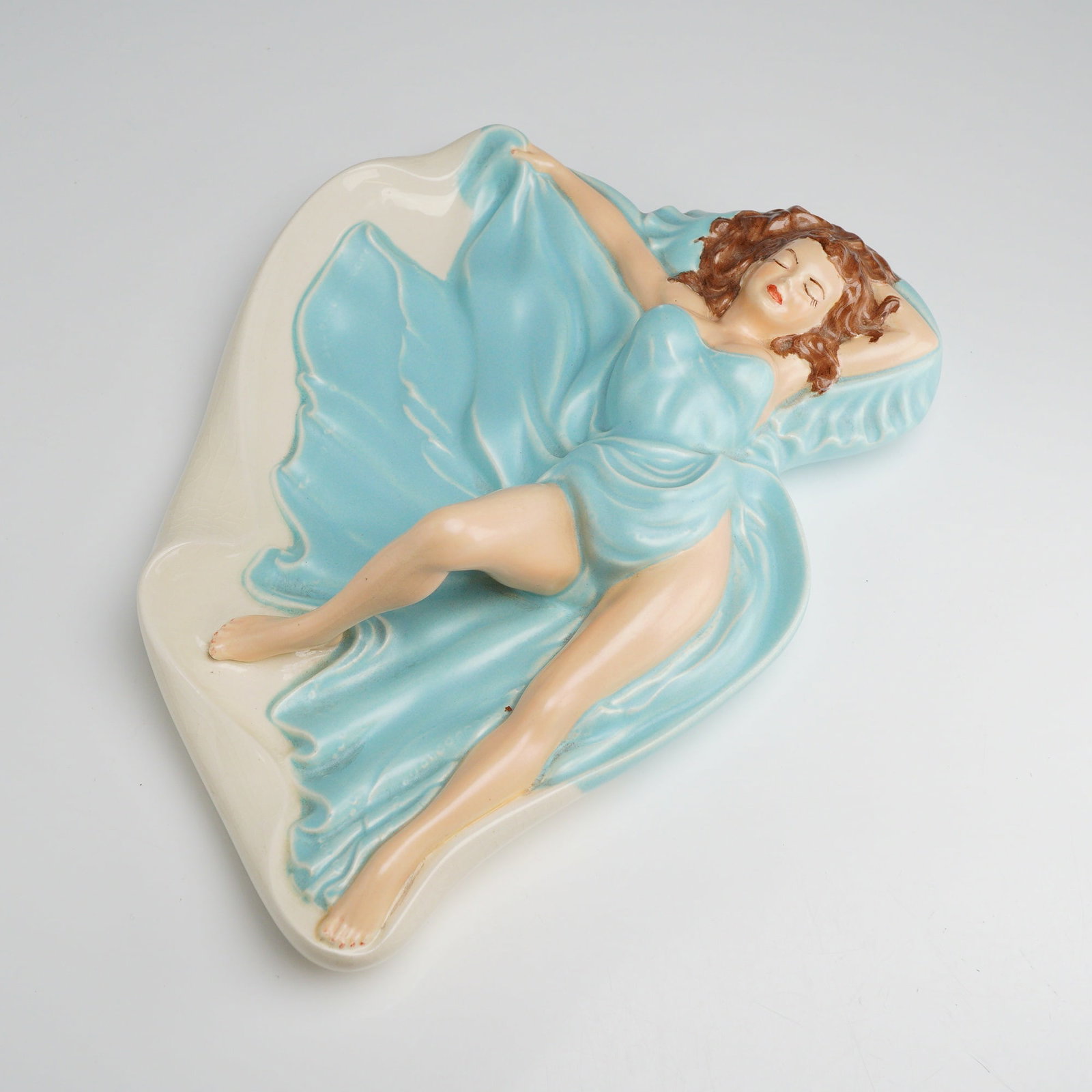 Mid-Century Ceramic Pin-up Style Girl in Blue Ashtray: A mid-century decorative ceramic console dish featuring a reclining female figure in a pin-up or glamour style. The figure is modeled with eyes closed and arms positioned behind her head, partially
