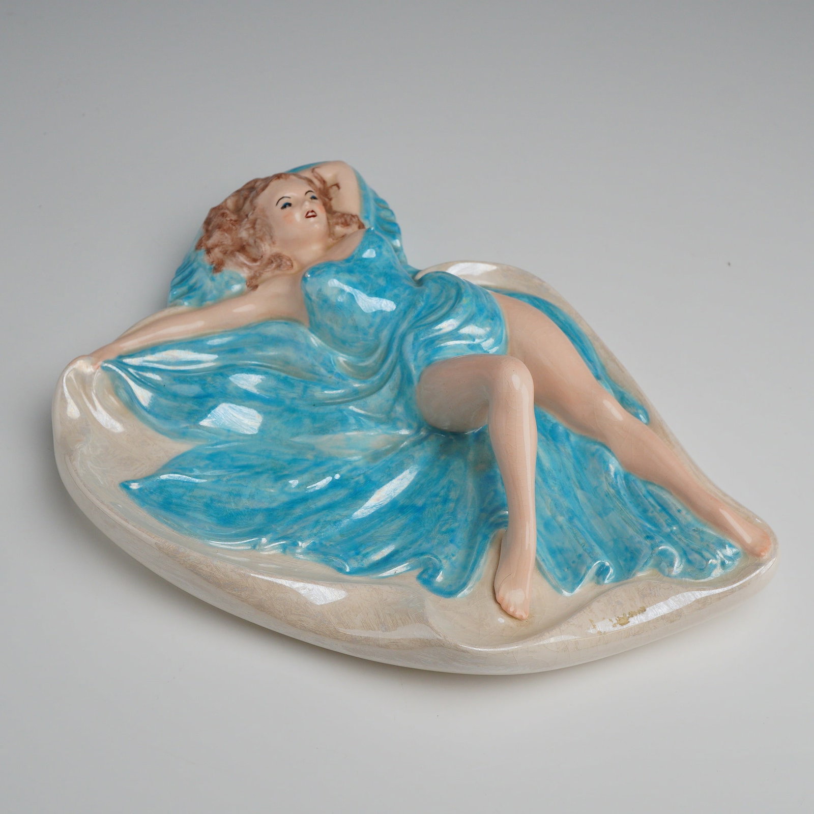 Mid-Century Ceramic Pin-up Style Girl in Blue Ashtray: This is a mid-20th-century glazed ceramic figural dish or ashtray produced by Holland Mold. The piece depicts a reclining pin-up style female figure with auburn hair, blue eyes, and red lips. She is