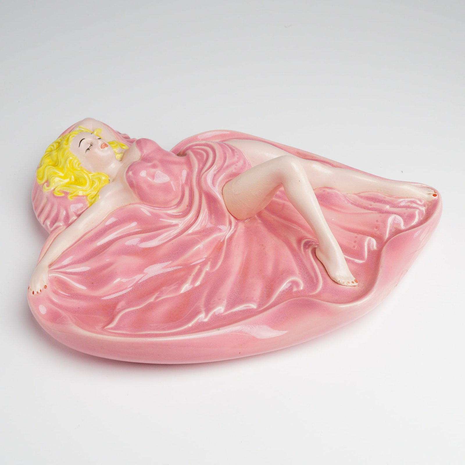 Mid-Century Ceramic Pin-Up Style Girl in Pink Ashtray, Marilyn Monroe: This mid-century modern ceramic ashtray is modeled as a reclining blonde pin-up figure, identified as Marilyn Monroe. The piece is constructed from hollow-cast glazed earthenware with a high-gloss fin