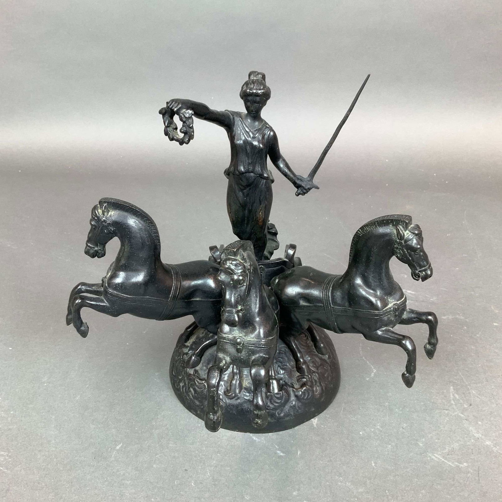 After Etienne-Henri Dumaige, Patinated Bronze Sculpture of Goddess Nike on Chariot: A neoclassical-style cast bronze sculpture depicting the goddess Nike, or Victory, standing in a triga chariot. The central figure is dressed in a classical chiton and holds a laurel wreath in her
