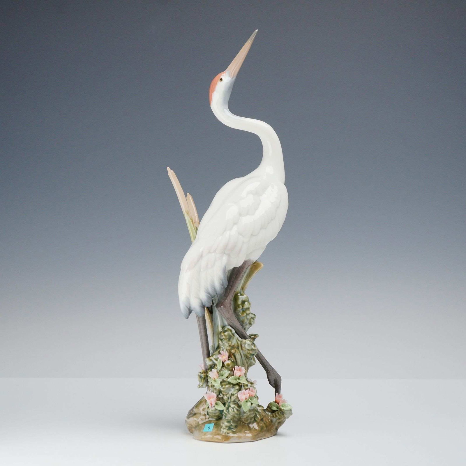 Lladro Porcelain Figurine, Dancing Crane 01001614: A glazed porcelain figurine produced by Lladro, titled Dancing Crane, model number 01001614. The sculpture depicts a white crane with a red crest and gray-toned wing tips, posed with its long beak poi