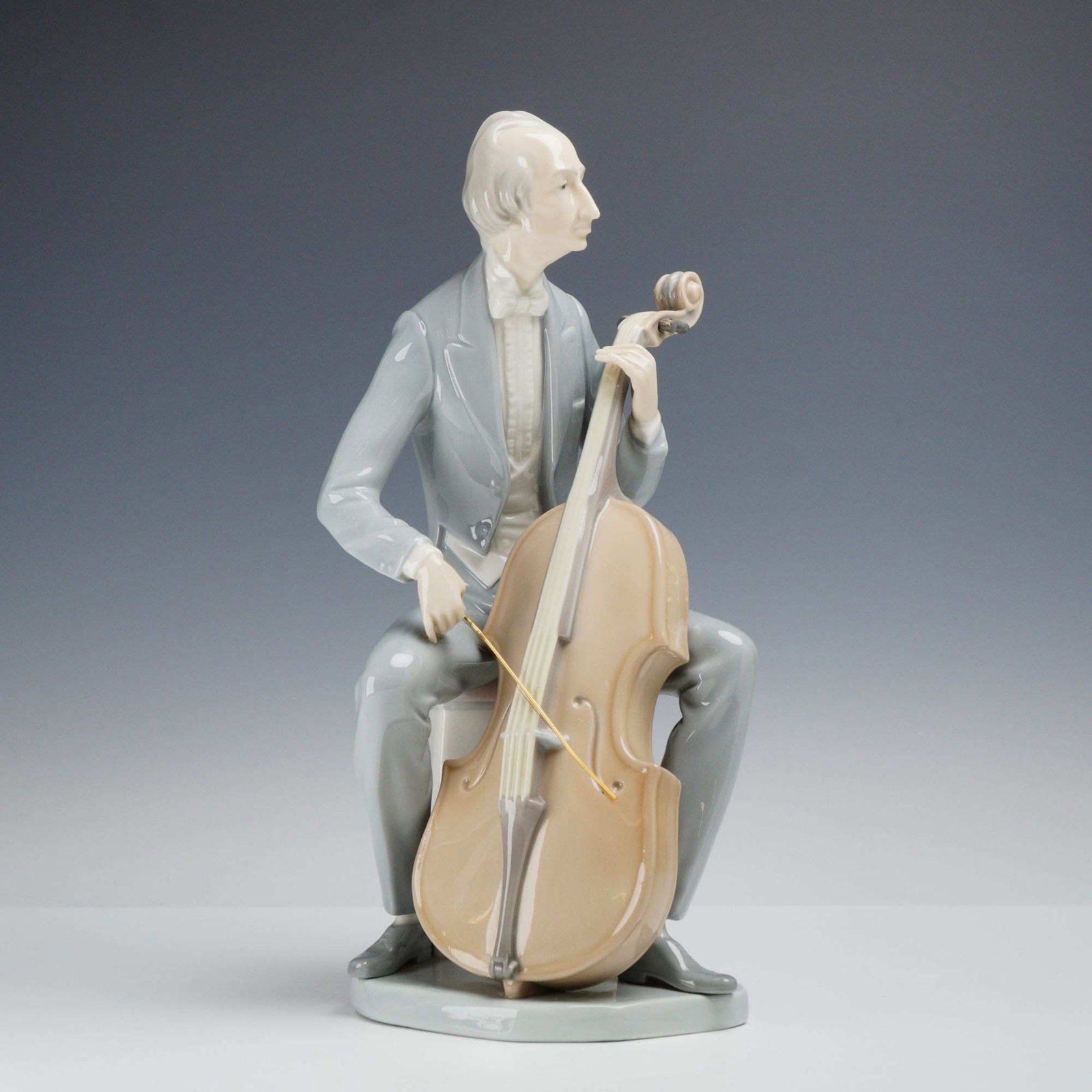 Lladro Glazed Porcelain Figurine, Cellist 01004651: A glazed porcelain figurine produced by the Spanish manufacturer Lladro, titled Cellist (Item #01004651). The piece depicts a male musician in formal morning dress, including a long-tailed grey coat, 