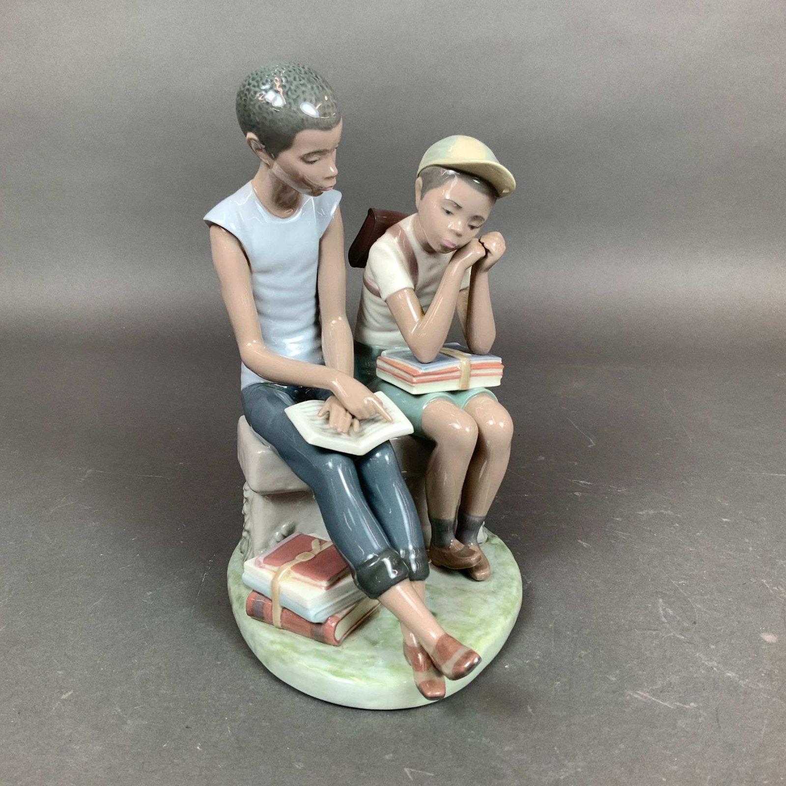 Lladro Black Legacy Porcelain Figurine, School Chums 01005237: This Lladro glazed porcelain figurine is identified as School Chums (item #01005237) and belongs to the Black Legacy collection. Designed by Salvador Furio, the scene depicts two young boys of African