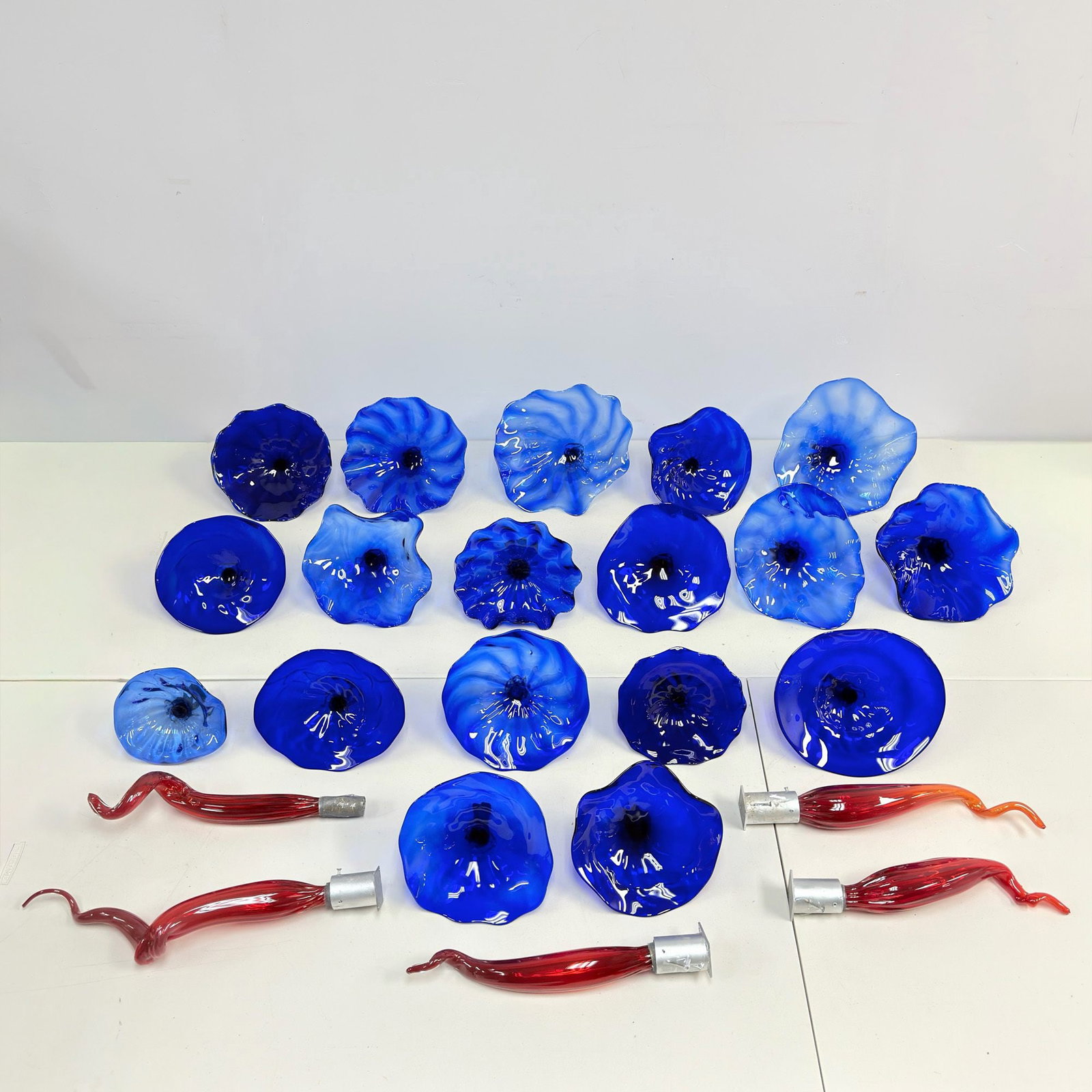 23pc Blown Art Glass Installation Components: This group consists of 23 blown art glass pieces designed for a large-scale sculptural installation. The set features 18 flower-form plates in various shades of blue, ranging from pale sky blue to dee