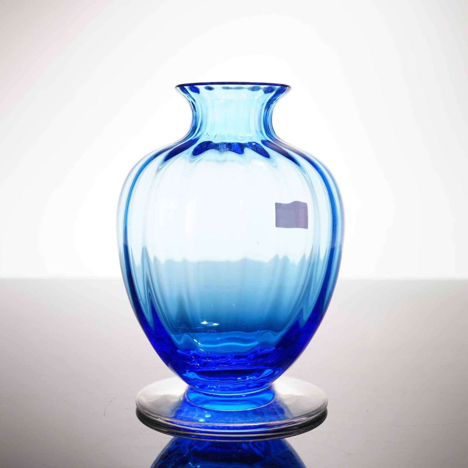 Baccarat Blue Aquarelle Crystal Bud Vase with Original Box: A Baccarat crystal bud vase in the Aquarelle pattern, featuring an optic-ribbed baluster-form body and a flared, undulating rim. The vessel exhibits a color gradation, transitioning from a translucent