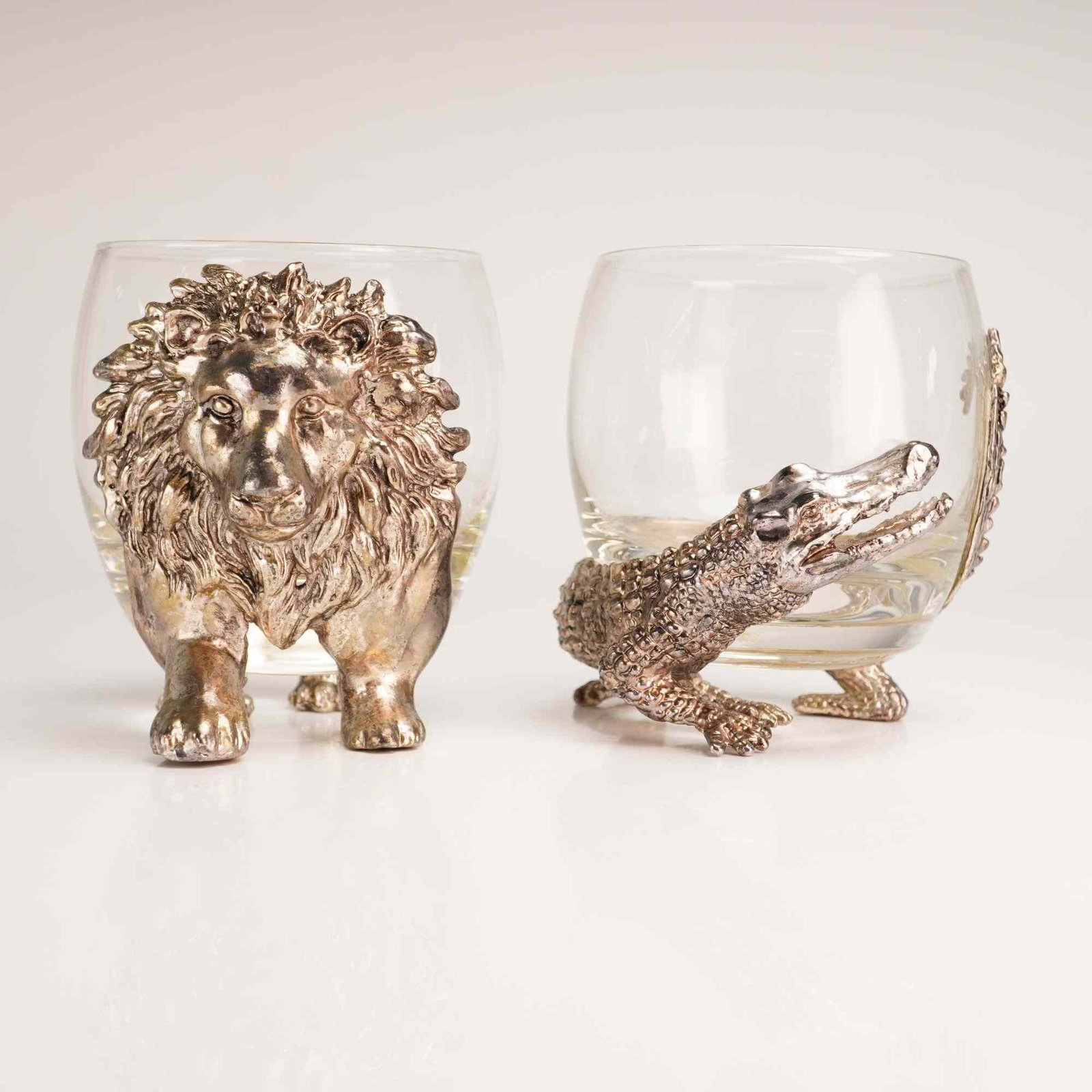 A Pair of Arthur Court Designs Pewter and Glass Safari Animal Figural Glasses: A pair of double old-fashioned rocks glasses featuring decorative, figural cast-pewter wraps and bases by Arthur Court Designs. One glass is designed with a lion motif, where the lion head and forepaw