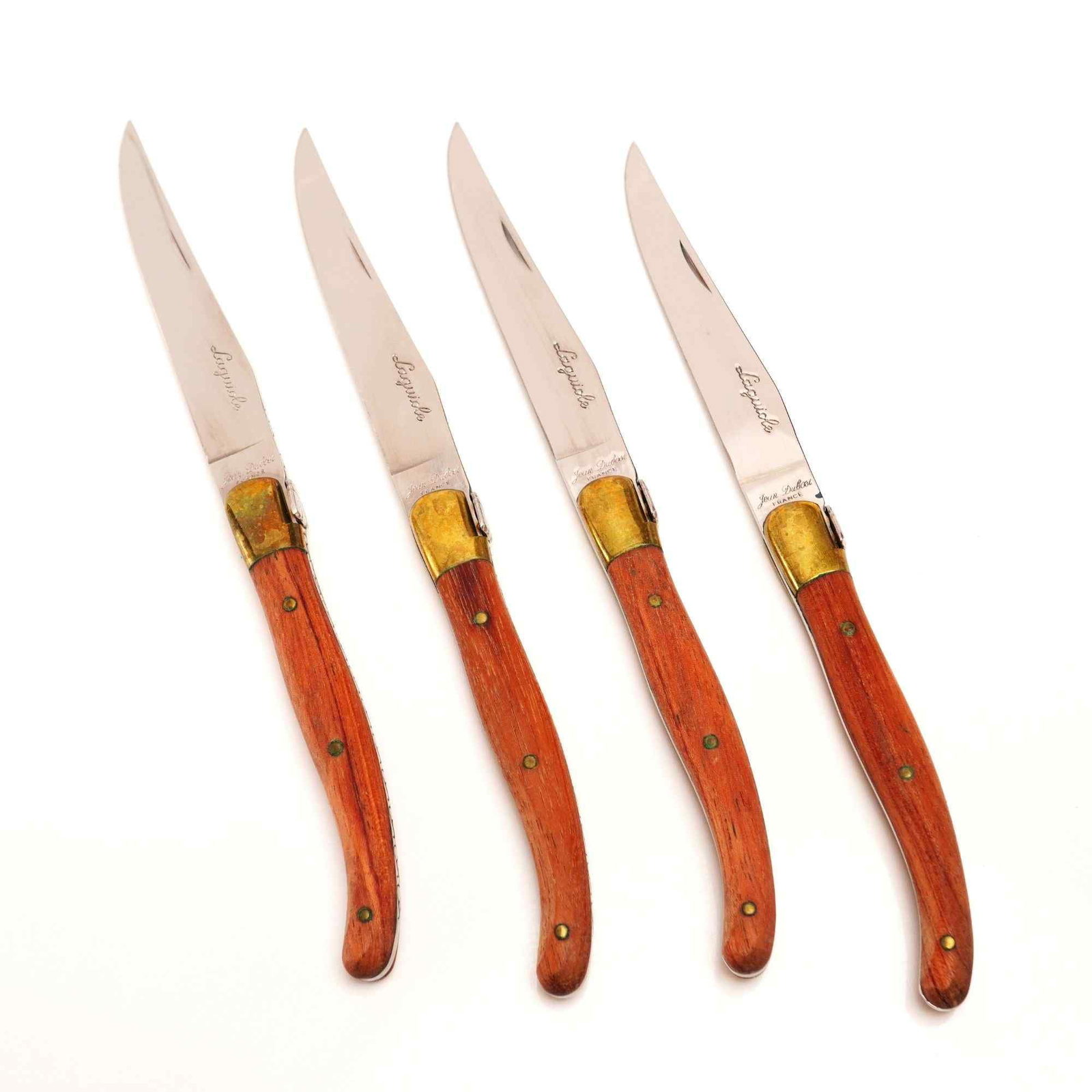 4pc Set of Jean Dubost Laguiole Steak Knives with Brass and Wooden Handles: A 4pc set of Jean Dubost Laguiole steak knives manufactured in France. Each knife is constructed with a curved stainless steel blade featuring a polished finish. The handles are made of wood, contoure