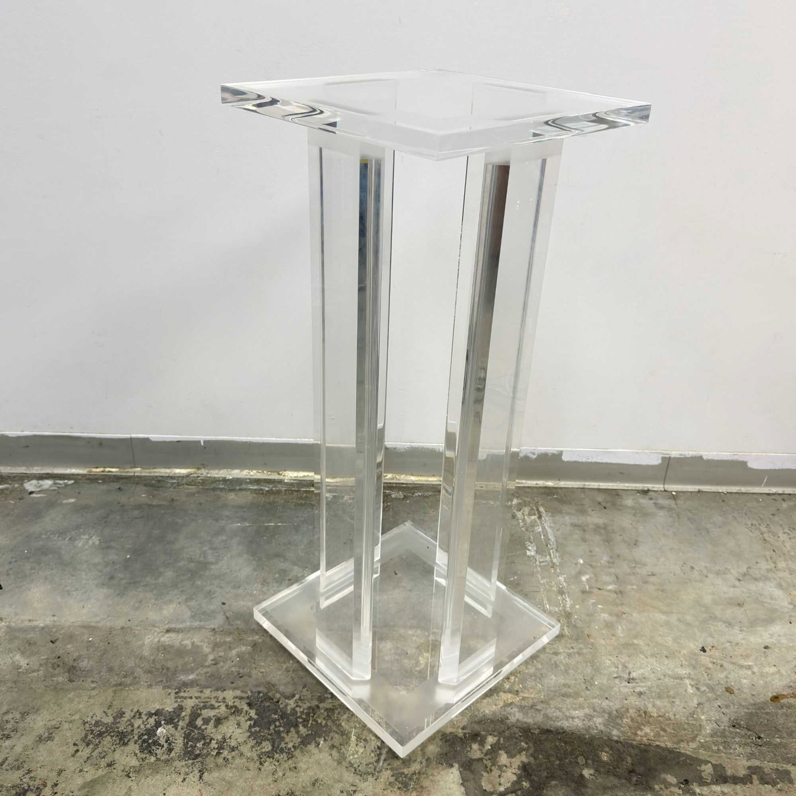 Modernist Lucite Pedestal Display Stand: This Lucite pedestal display stand is constructed from thick, clear acrylic in a modernist design reminiscent of the late 20th-century Hollywood Regency revival. The stand consists of a square top wit